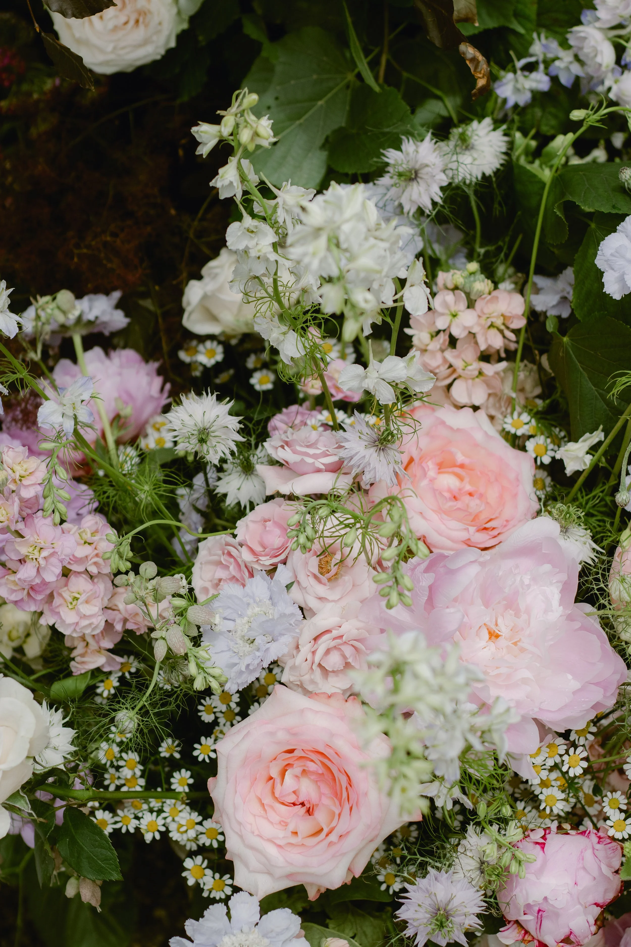 A vibrant assortment of blooming flowers including pink roses, white peonies, daisies, and other delicate flowers in various shades of white and pink.