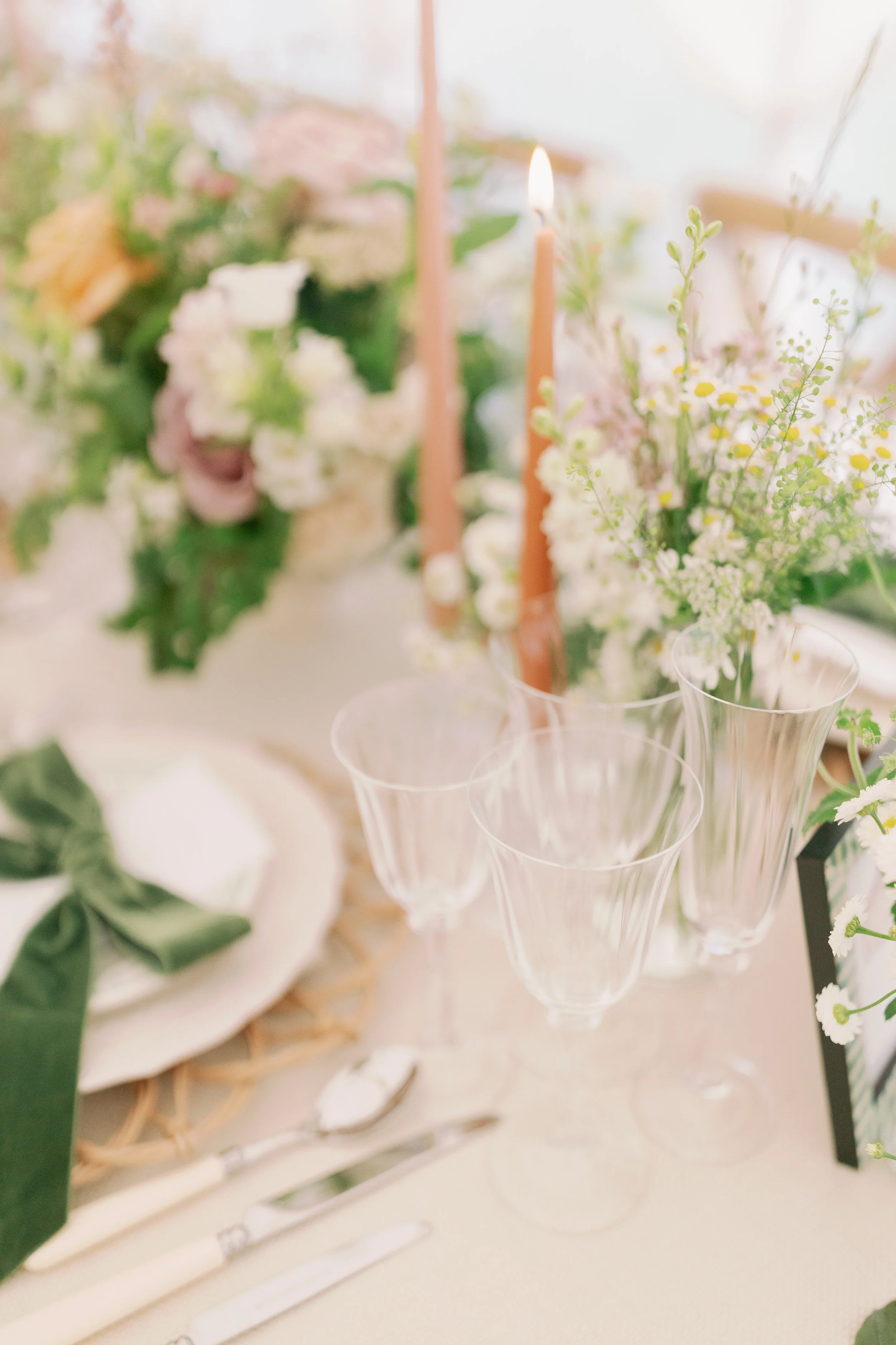 A close-up of a table setting with floral arrangements, and lit candles in a bright and elegant sailcloth marquee in Norfolk