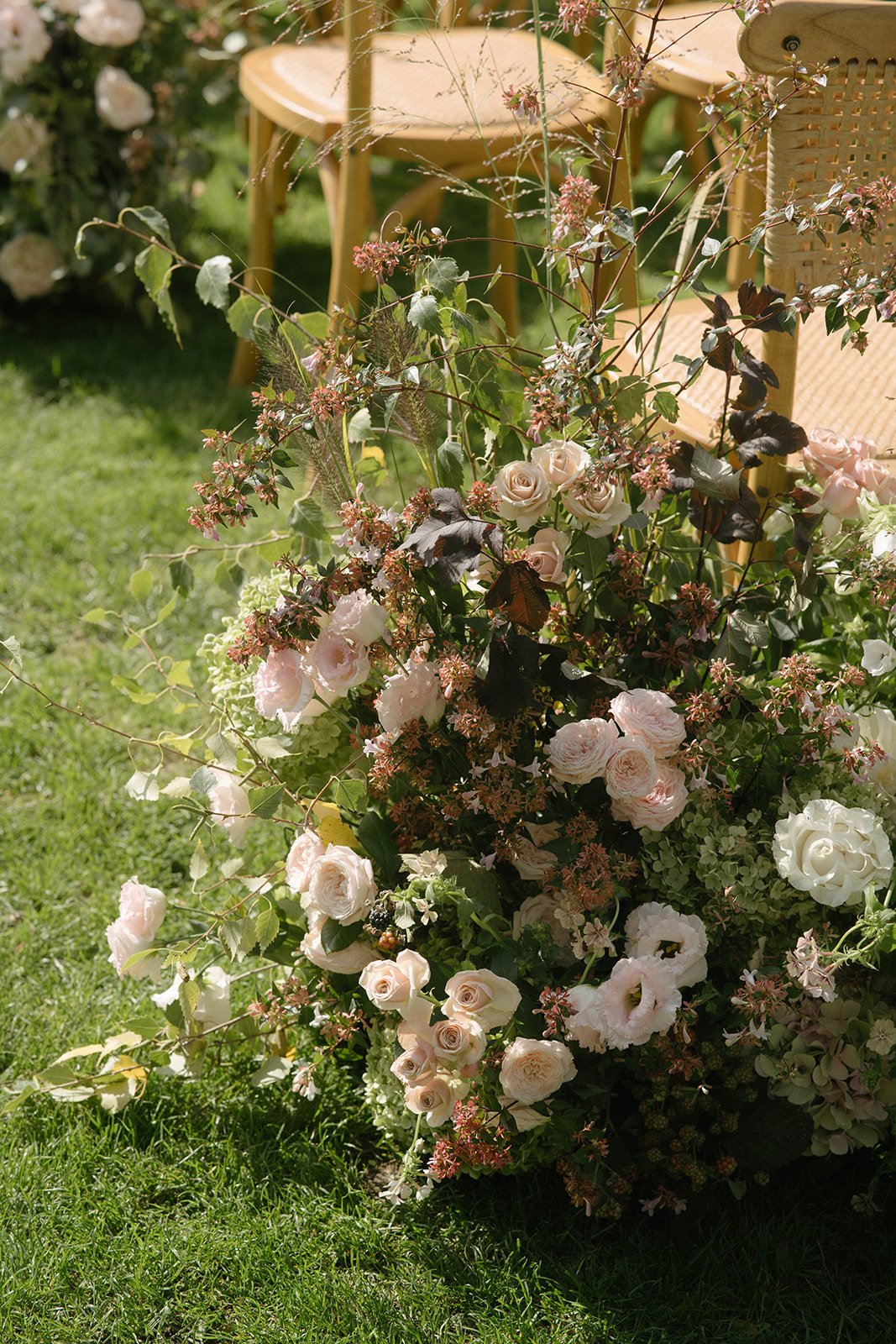 A luxury garden-style floral arrangement of blush and cream roses with verdant greenery at Cornwell Manor, styled for an outdoor wedding ceremony by The Botany House wedding florist.