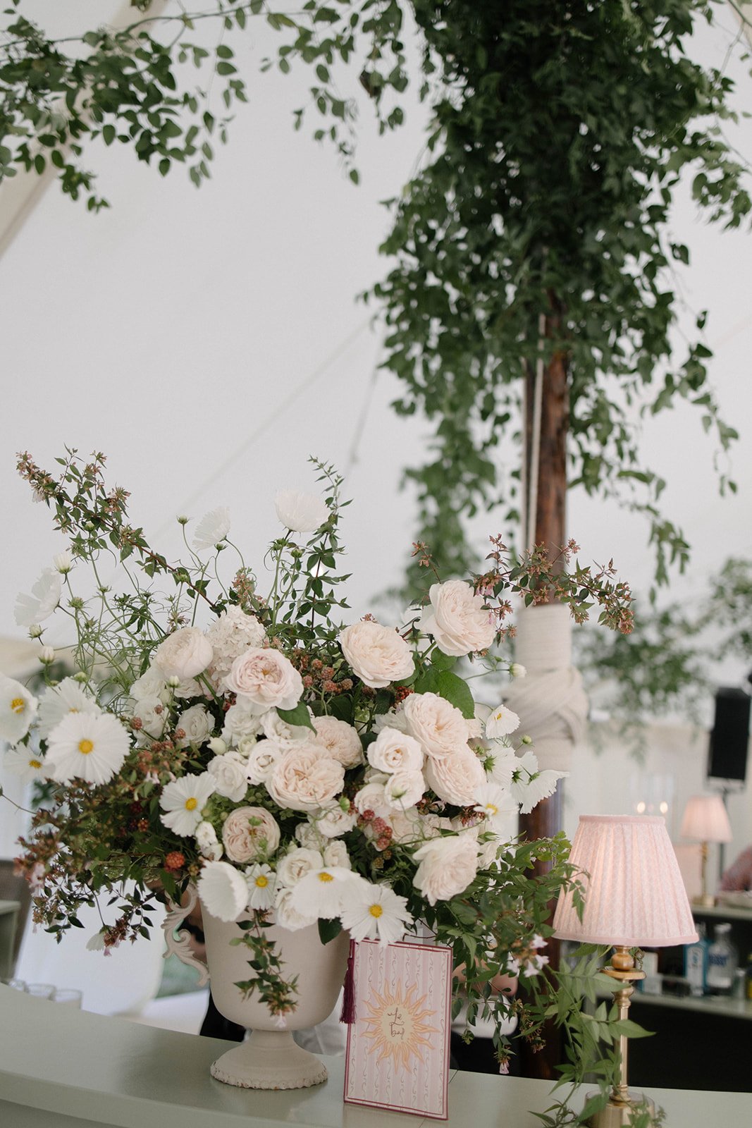 White rose and daisy table arrangement in a decorative vase with pink lamp details at a Cornwell Manor wedding styled with luxury garden style floristry by The Botany House