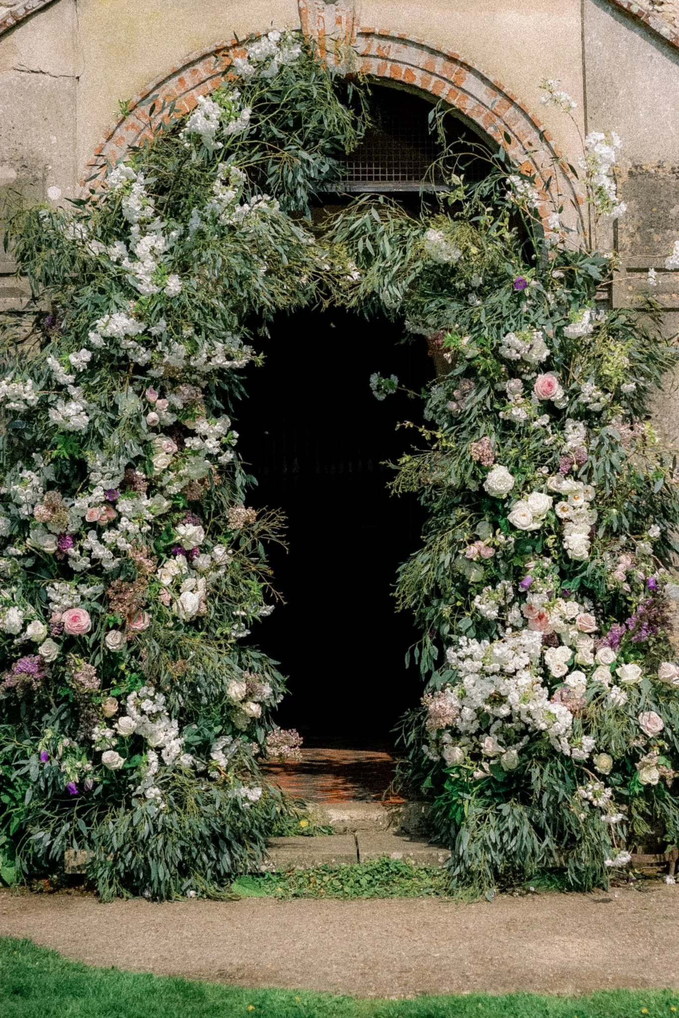 A doorway decorated with a floral arch made of various white and purple flowers and greenery.