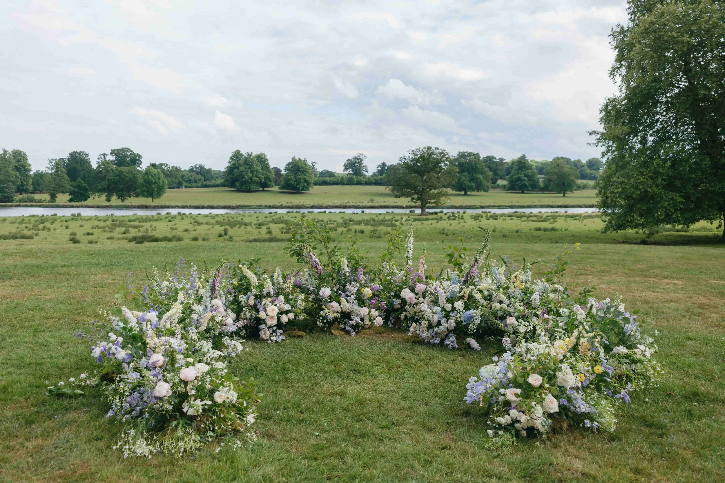 Meadow-style floral archway in lilac, blush, blue and yellow at English countryside wedding ceremony at Wilderness Reserve