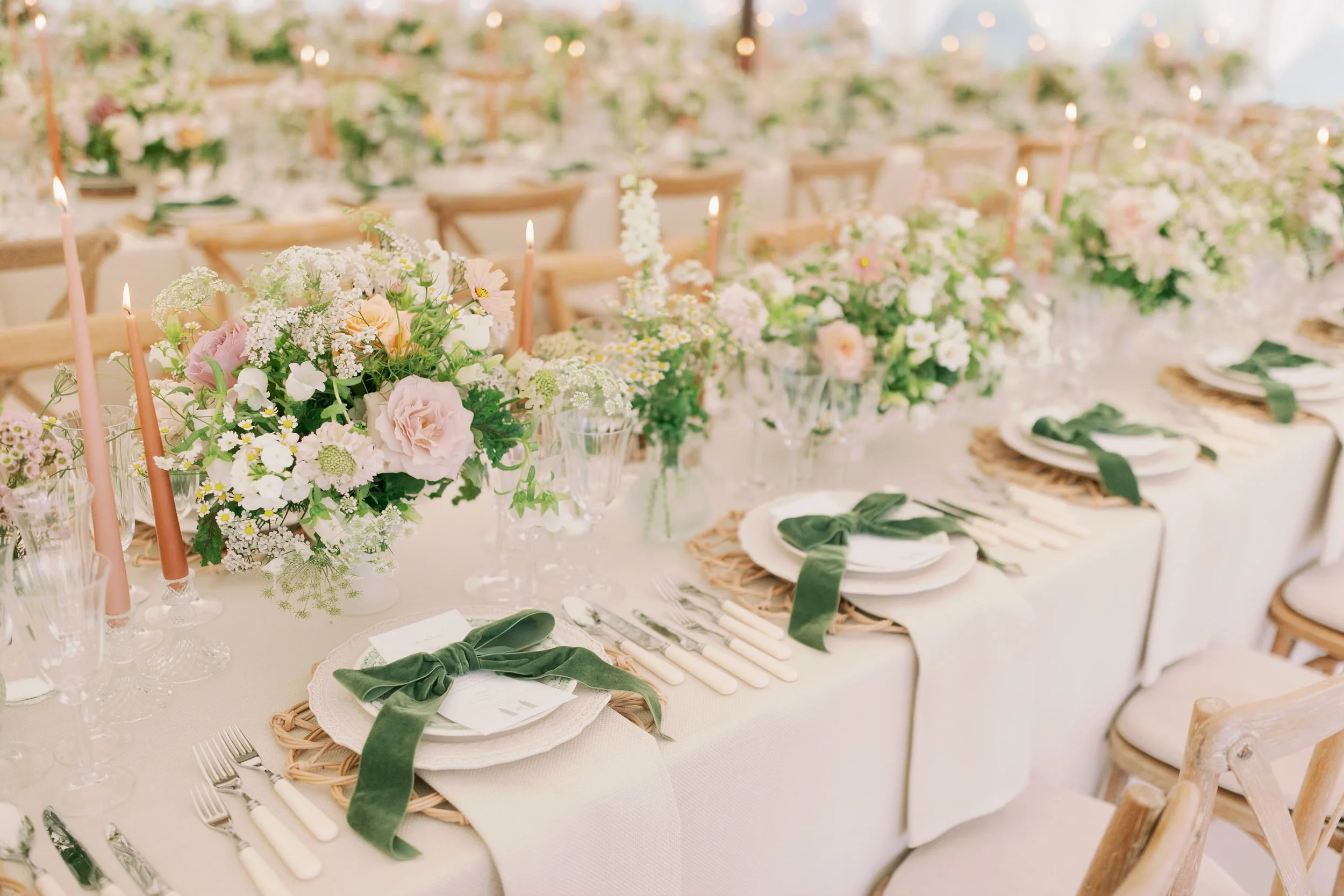Elegant wedding reception table with floral centerpieces, candles, and arranged place settings with plates, silverware, and green velvet bows. Hosted in Norfolk