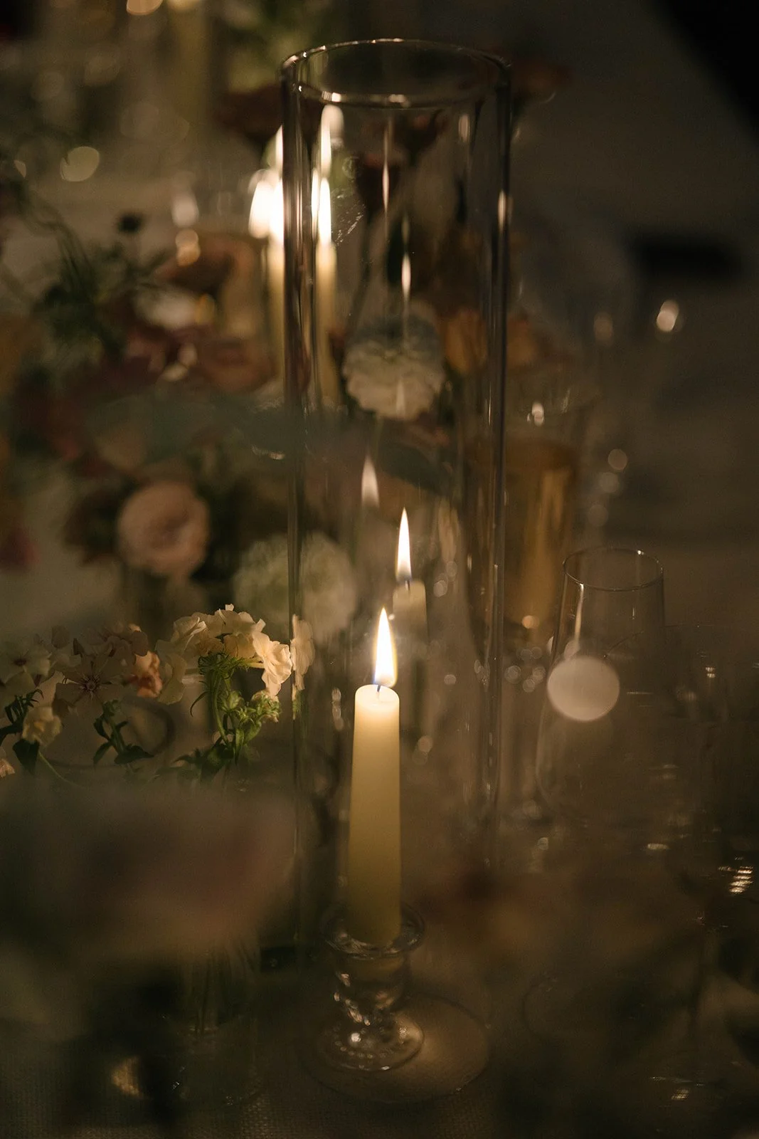 Lit candle in a glass holder on a Cornwell Manor wedding table surrounded by soft floral styling by The Botany House wedding florist
