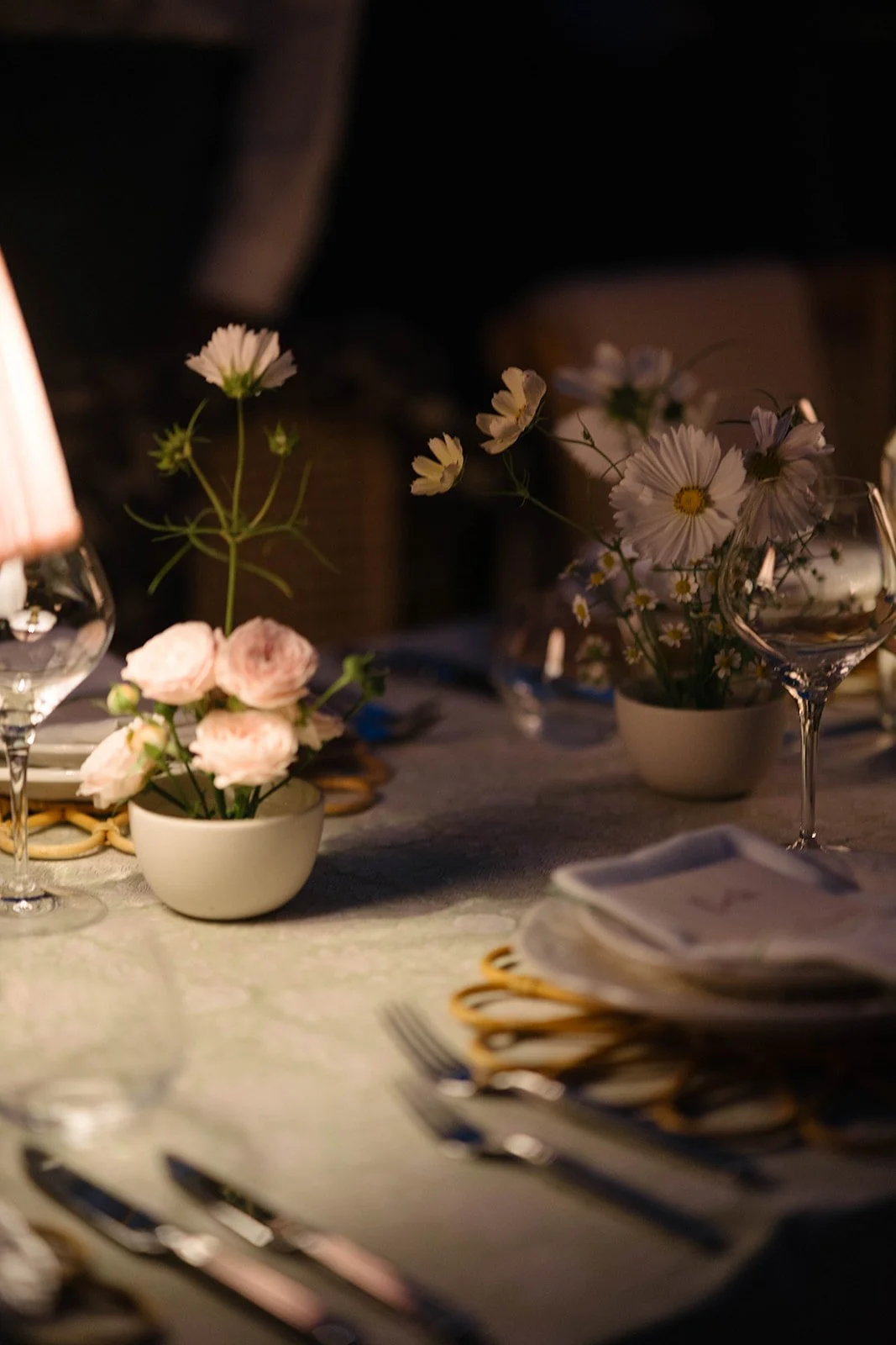 A table decorated with small floral arrangements in white bowls, featuring pink roses and white daisies, set for a rehearsal dinner -  luxury garden-style wedding flowers by The Botany House, Cornwell Manor specialising in romantic marquee florals