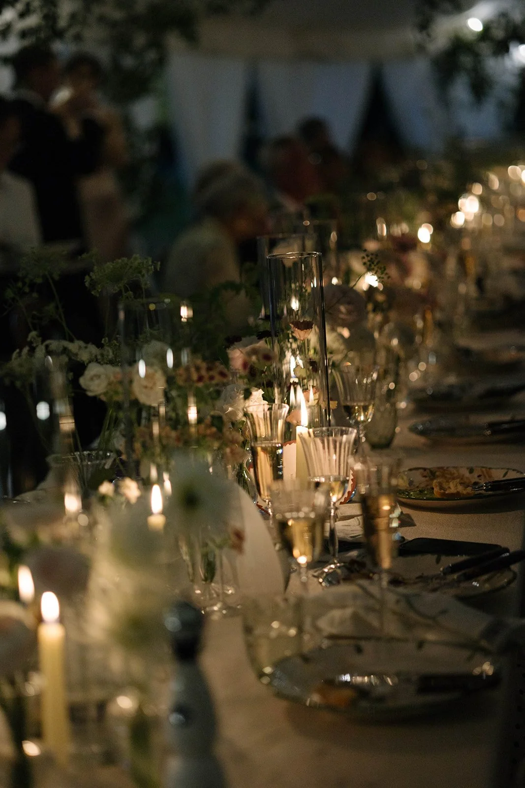 Dimly lit Cornwell Manor wedding table with flowers candles and glassware styled with bespoke luxury wedding floristry by The Botany House