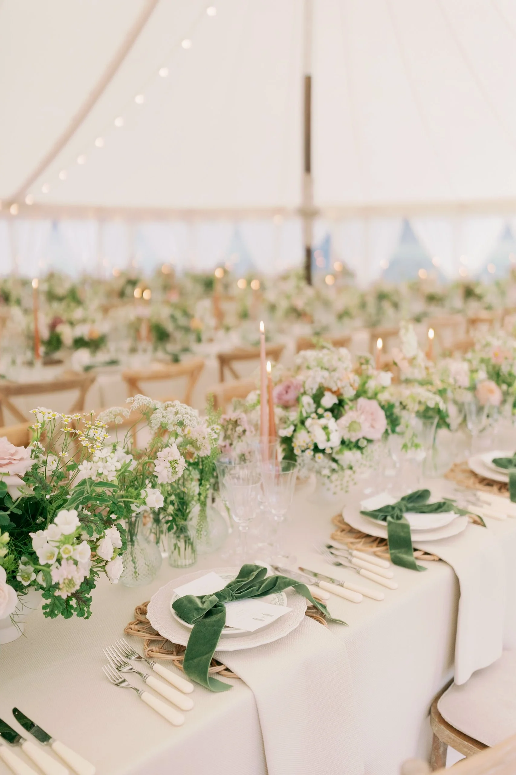 Elegant wedding table decorated with fine art floral arrangements, green bow accents and tall candles under a large marquee