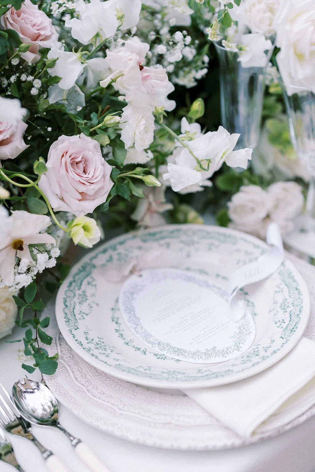 A table setting with a white and green floral centerpiece, floral-patterned plates, and silverware.