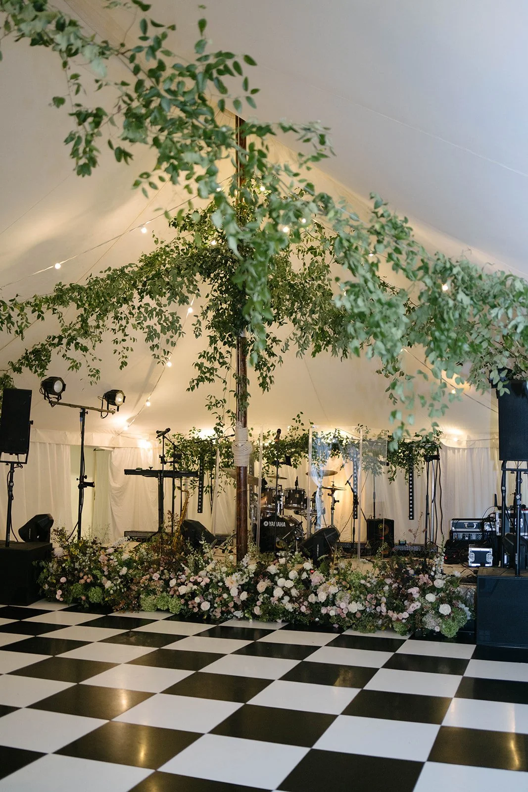 Stage inside a sailcloth marquee at Cornwell Manor with ceiling foliage installation and floral styling over a black and white floor styled by The Botany House wedding florist