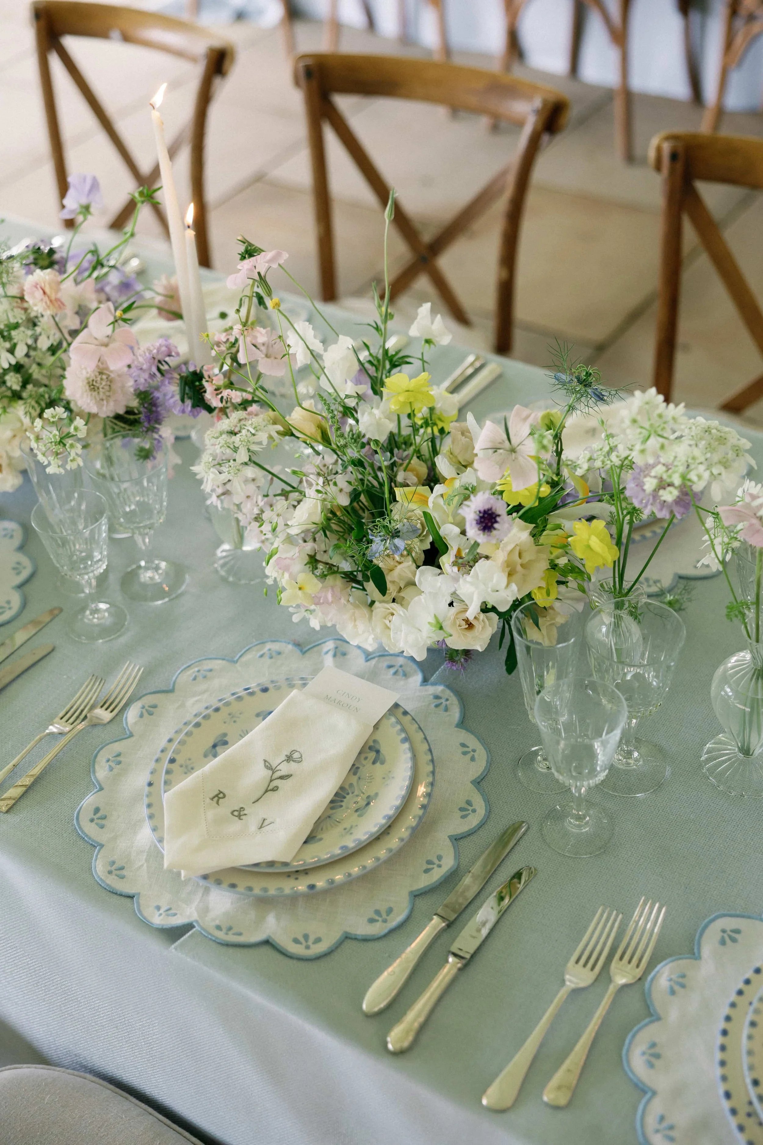 A decorated table for a special occasion with floral centerpiece, gold cutlery, patterned plates, glassware, and a name card with initials R & V in an elegant setting. Wilderness Reserve, Suffolk Florals By The Botany House
