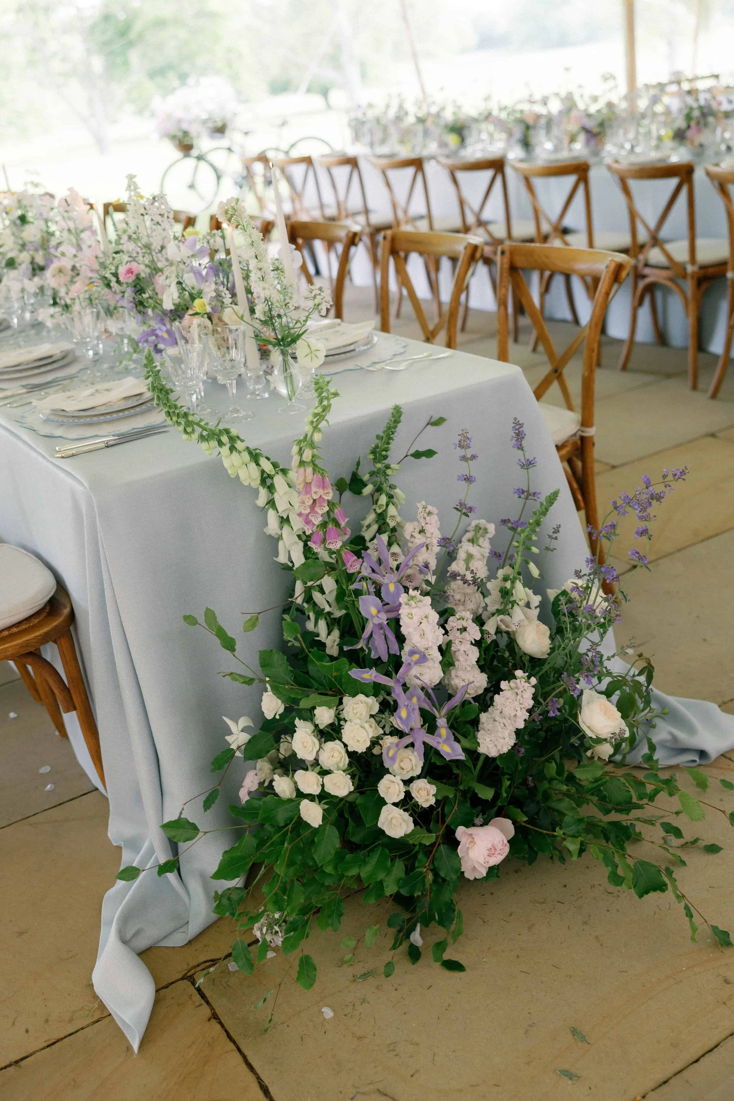 Elegant event table decorated with pastel flowers and glassware, set against a backdrop of a large window with outdoor view.