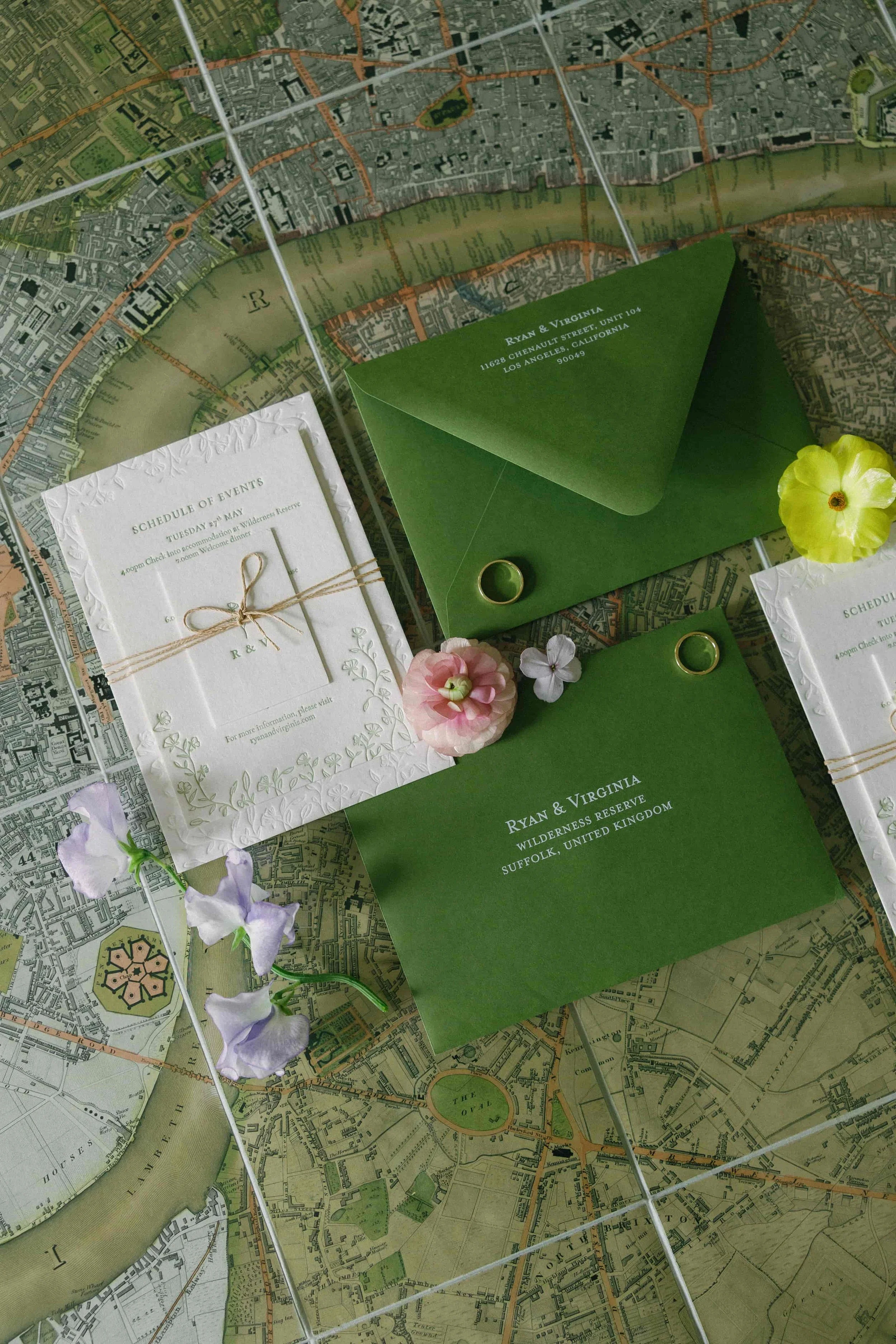 Wedding invitation stationery with green envelopes, floral decorations, and rings on a floral background. Wilderness Reserve, Suffolk Florals By The Botany House