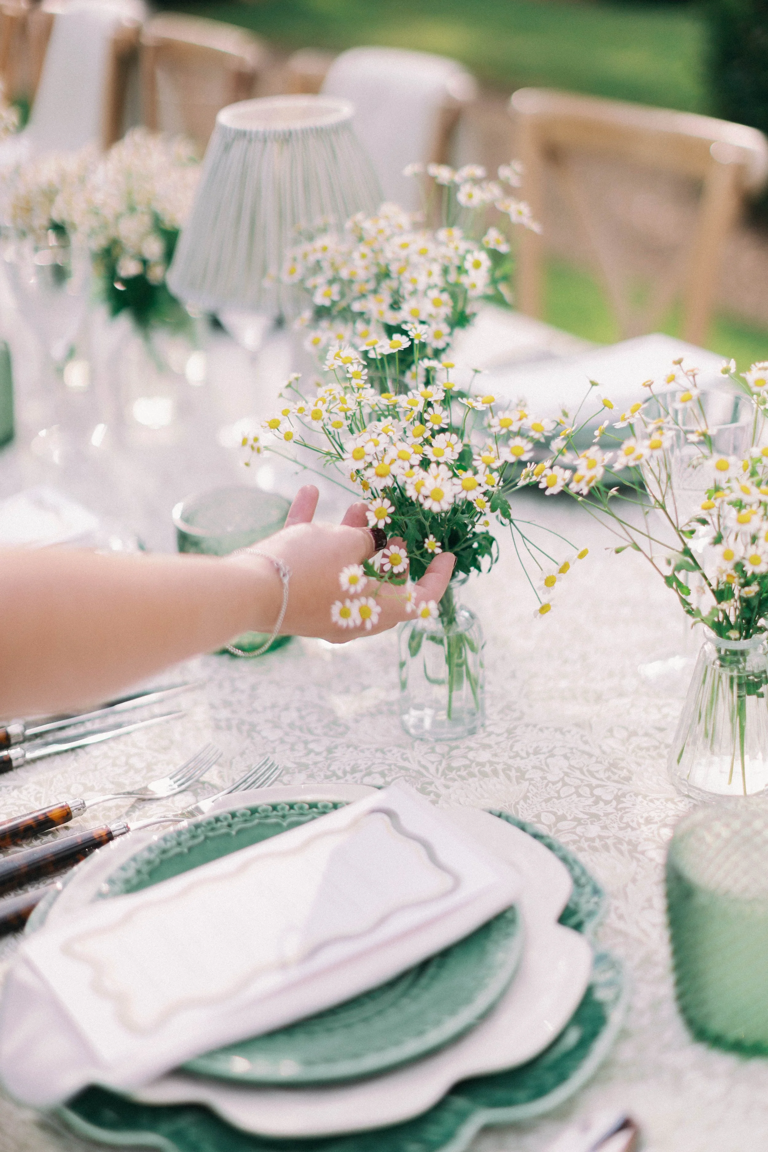A person is placing a small bouquet of daisies on a decorated table set for a rehearsal dinner.