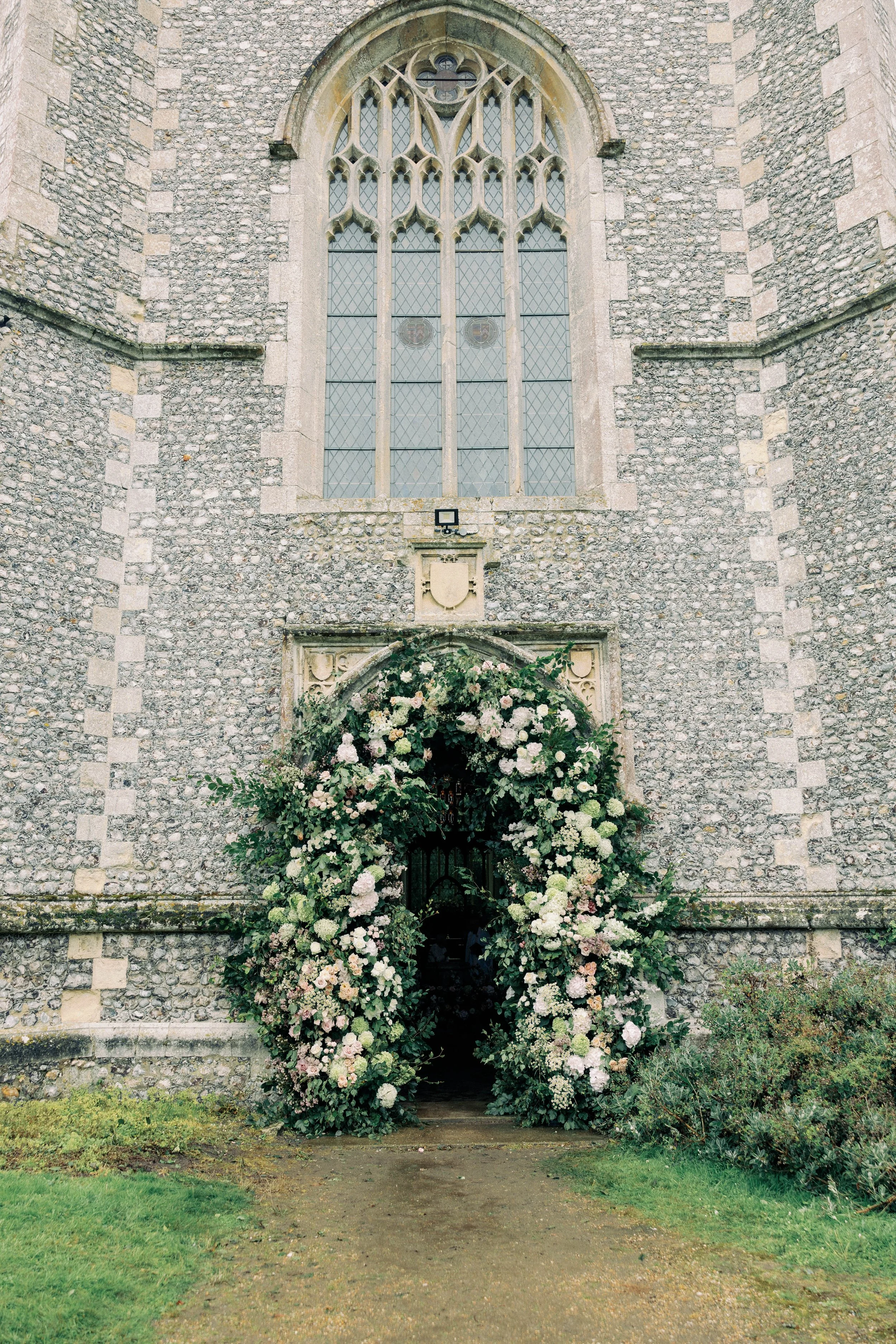 The entrance of a historic stone church in Heydon Norfolk. Decorated with a large floral archway installation ready for a wedding ceremony
