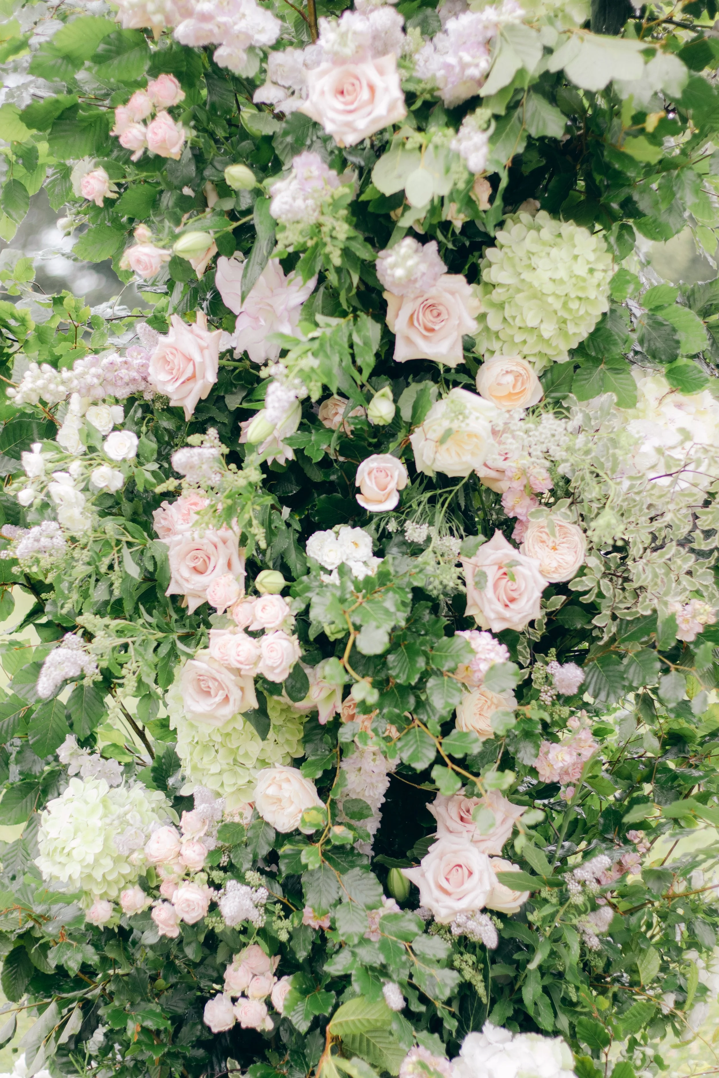 A dense arrangement of pastel pink roses, white hydrangeas, and various green foliage.