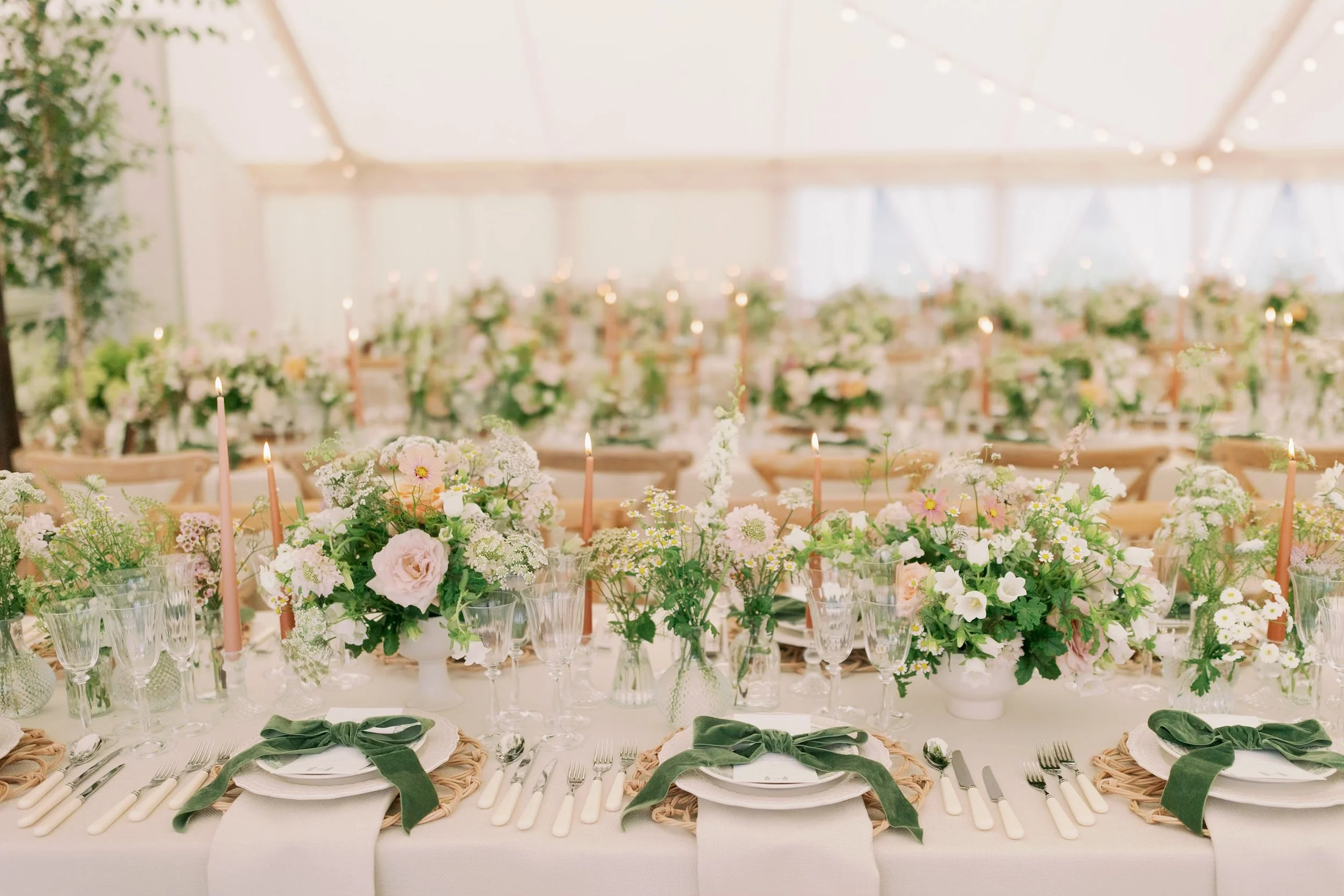 Elegant wedding reception table decorated with pastel flowers, candles, glassware, and green bows in a bright, airy sailcloth marquee in Norfolk