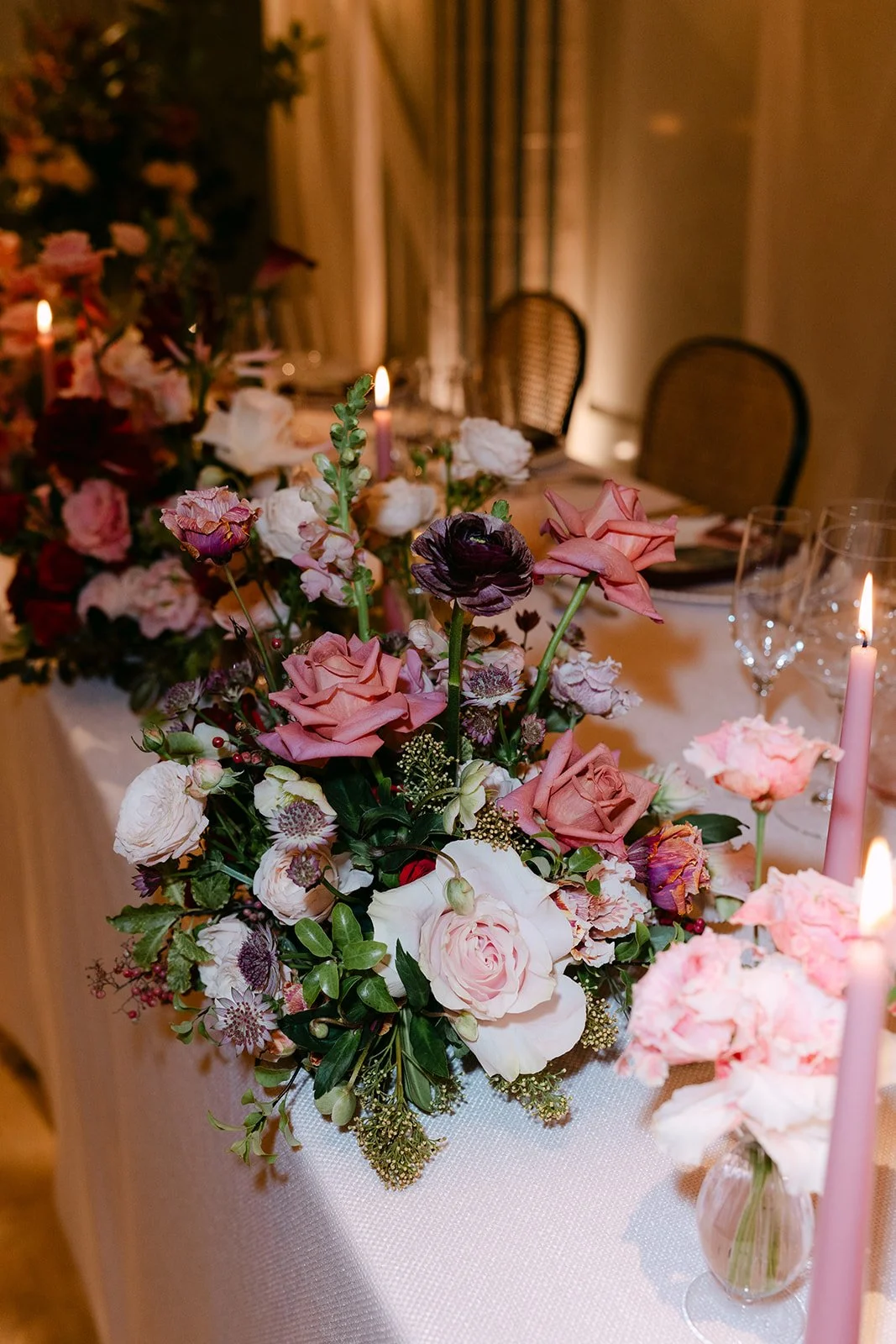Elegant dining table decorated with large floral arrangements and pink candles in a dimly lit room.