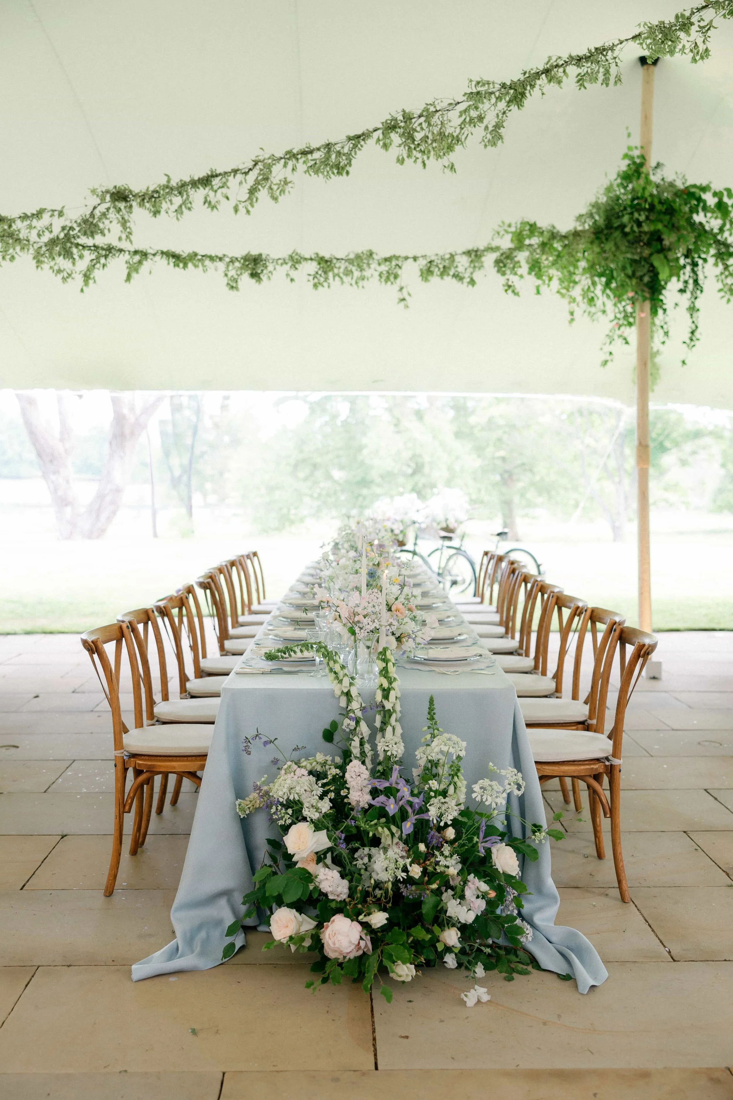 A long dining table set for a wedding or special event under a tent with green drapery and floral arrangements. The Botany House Florist at Wilderness Reserve, Planned by Attabara 