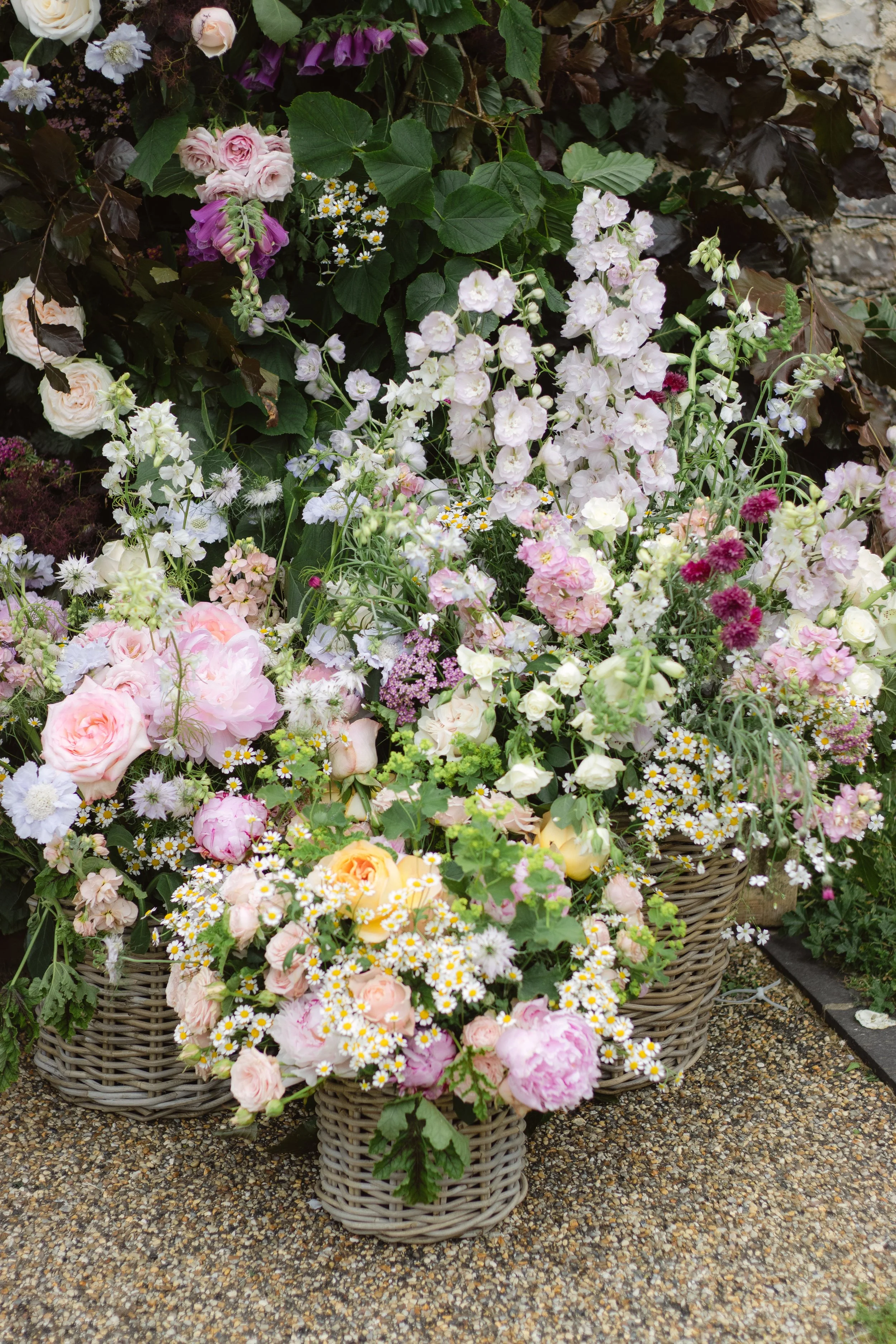 Brightly colored mixed flowers in various sizes and shapes arranged in woven baskets on a stone pathway.