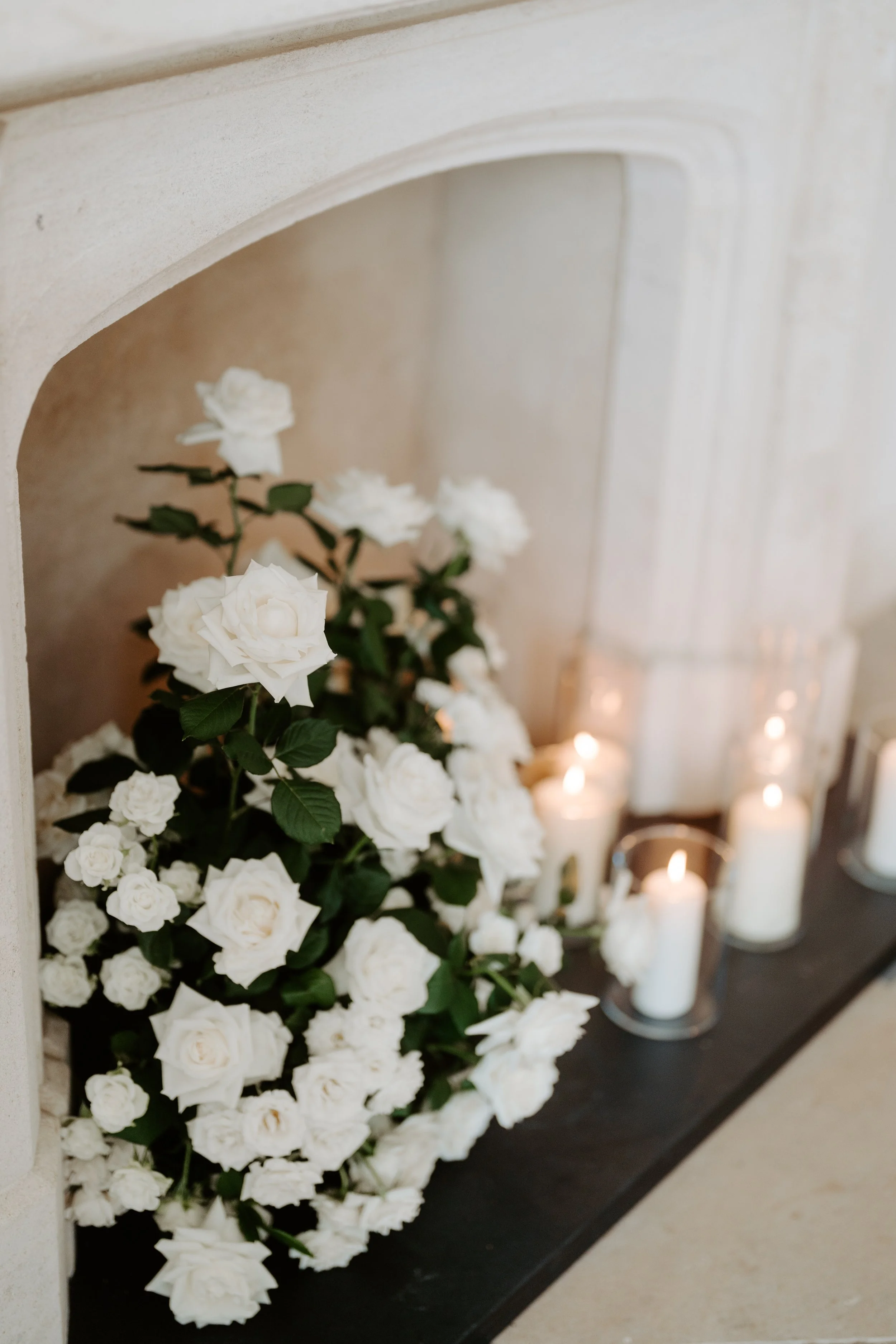 White roses and candles arranged on a mantelpiece.