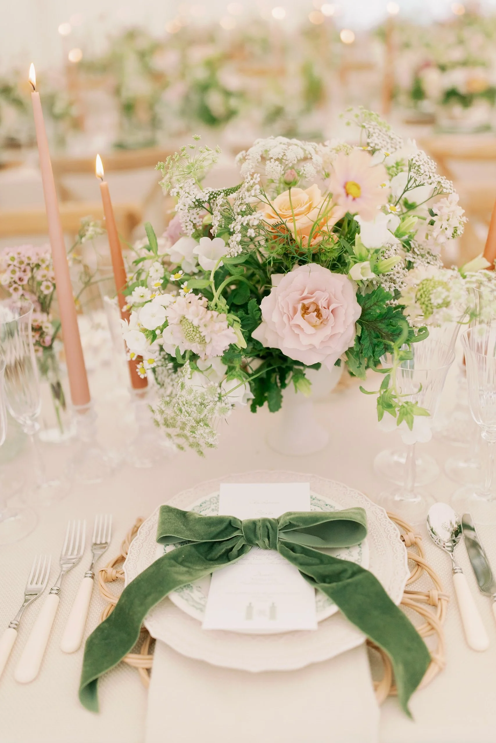 Elegant table centerpiece with pink, apricot and white flowers, surrounded by candles and glassware at a wedding reception.