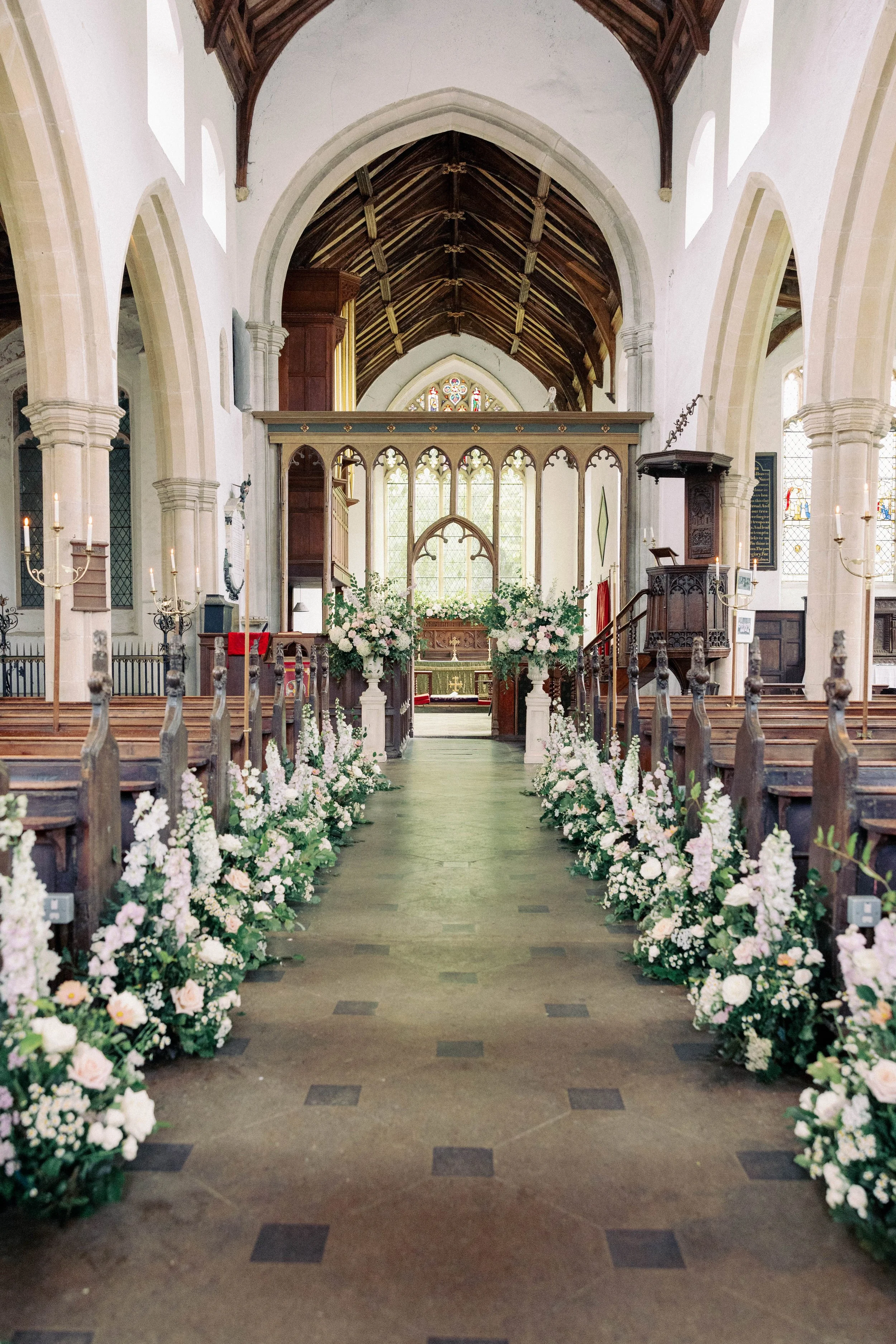 Interior of a church decorated for a wedding with floral arrangements along the aisle leading to the altar.
