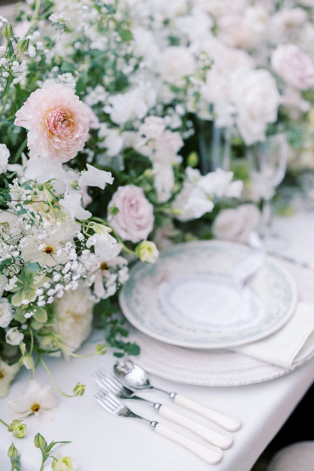 Elegant table setting with white and pink flowers, fine china, and silverware.