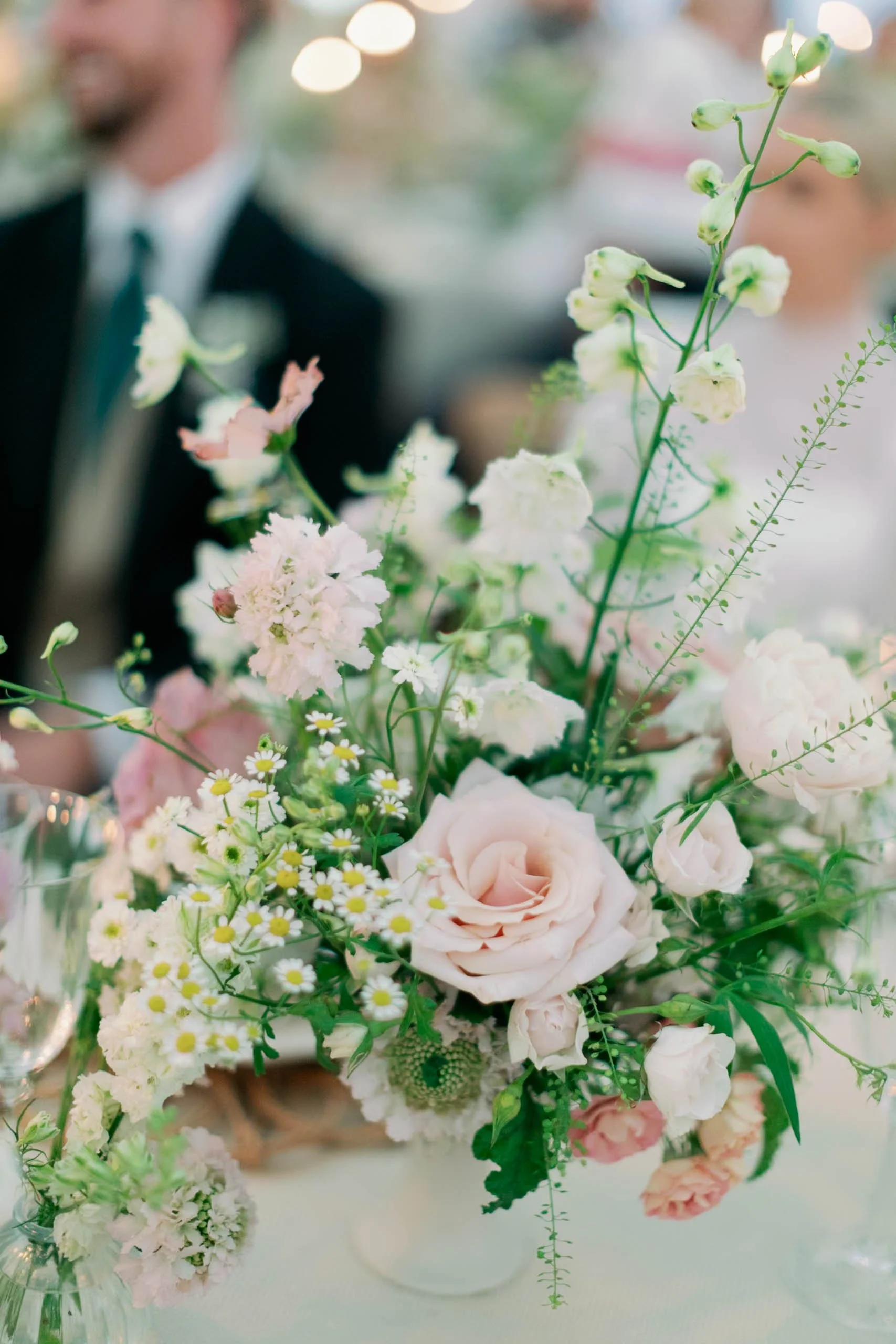 A floral centerpiece with white and pale pink flowers, including roses and daisies, on a table at a private home wedding in Norfolk