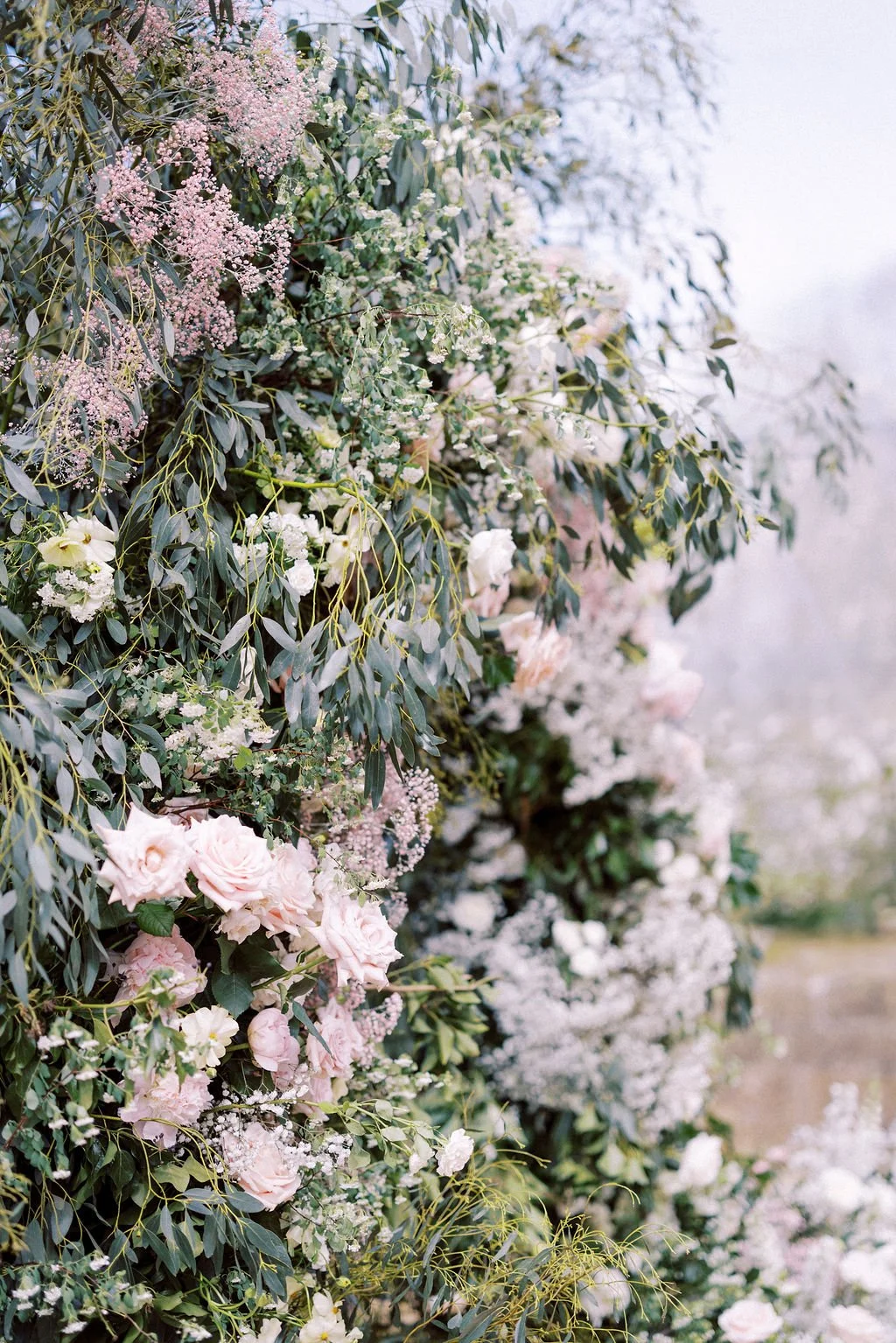 A vertical arrangement of pink and white flowers with green leaves, creating a lush floral display.