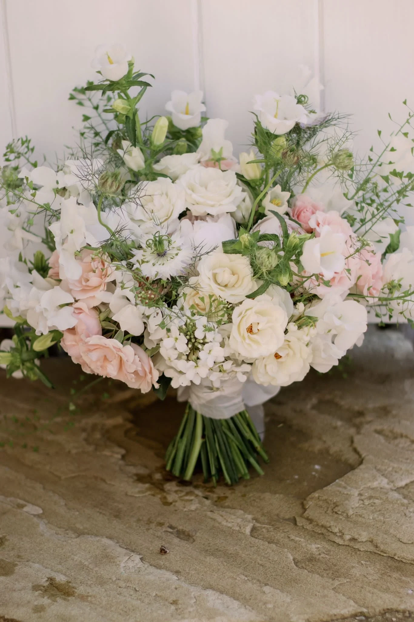 Bouquet of white and light pink flowers with greenery, arranged on a wooden surface.