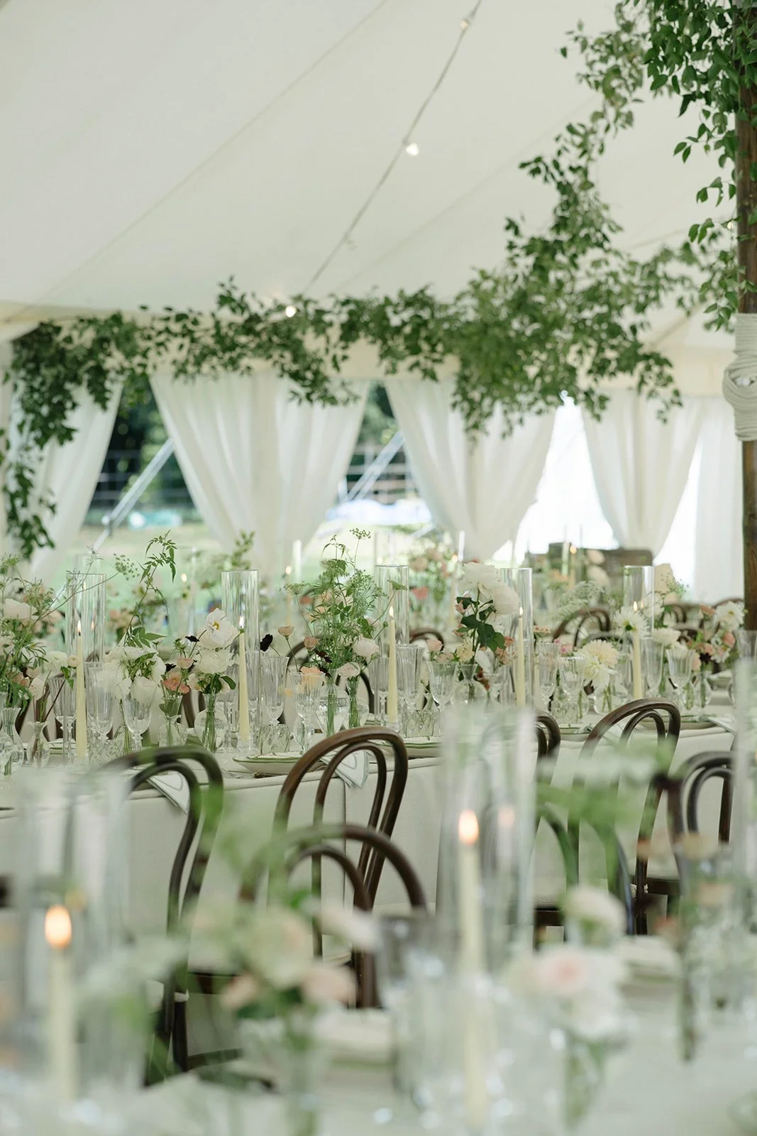 Elegant sailcloth marquee dining at Cornwell Manor with white linens floral centrepieces candles and greenery styled by The Botany House wedding florist