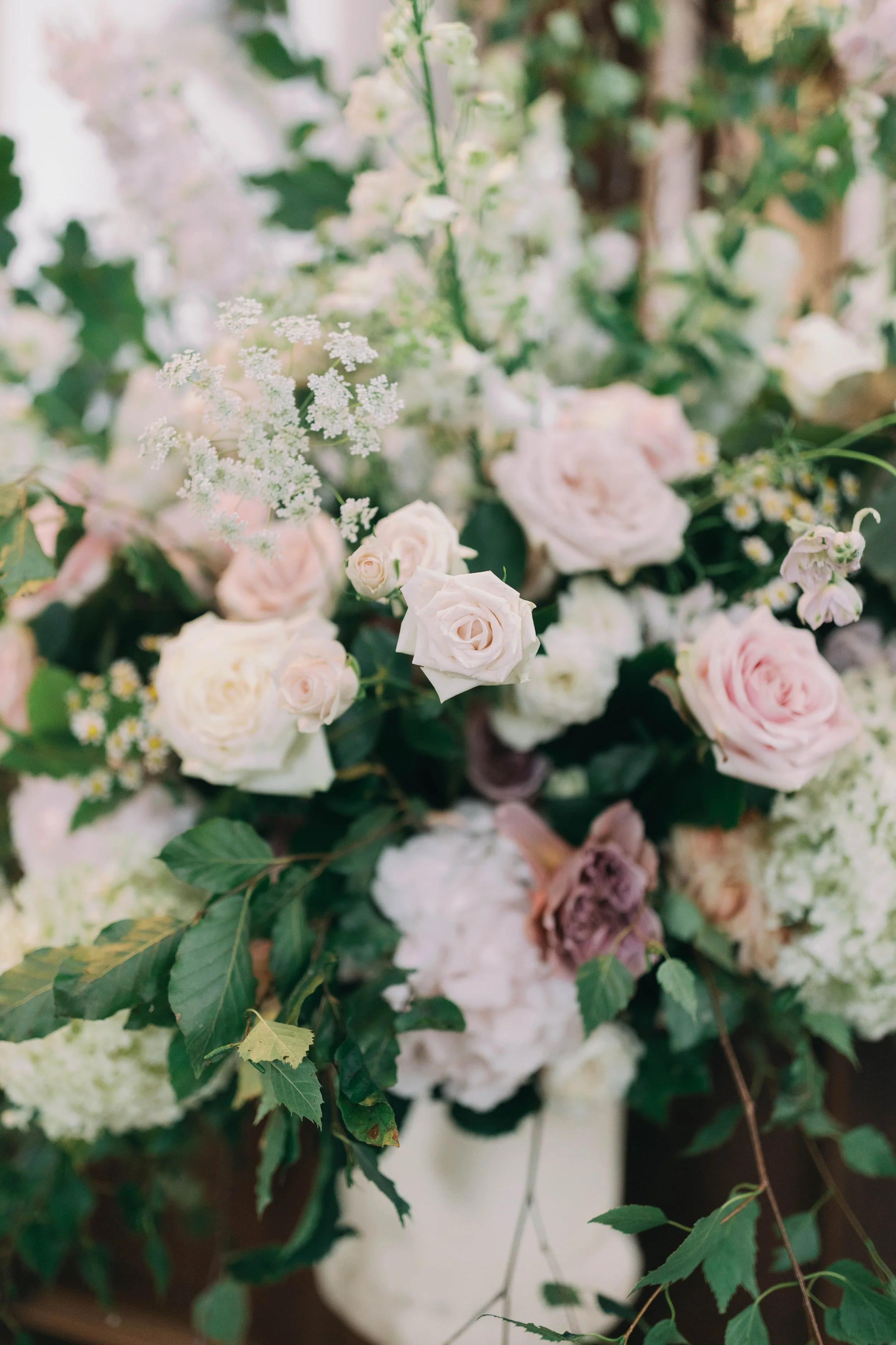 an urn full of of white, pink, and cream roses with green leaves and small white filler flowers in a village church in Norfolk.