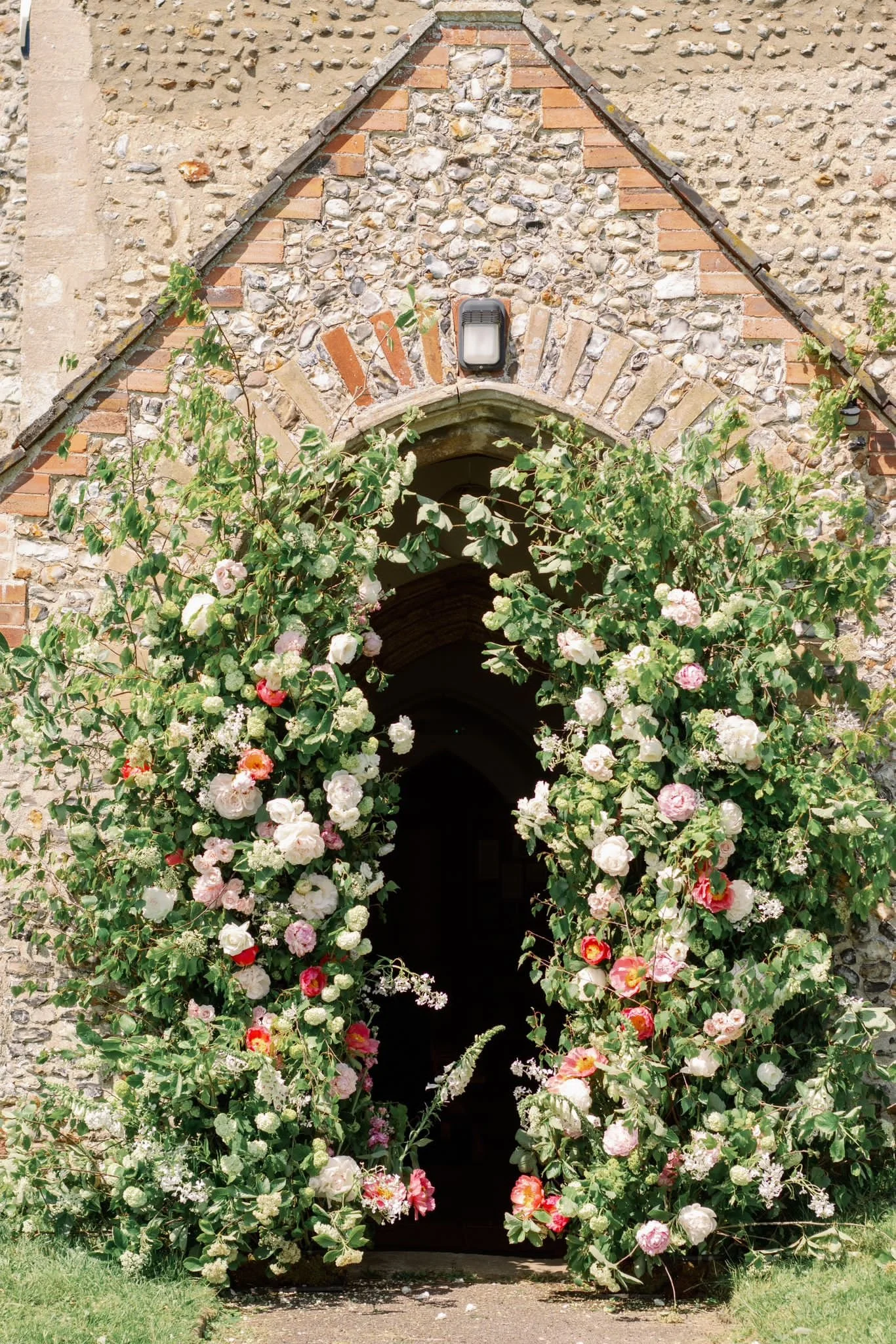 A stone church entrance decorated with lush, colorful flowering bushes and plants.