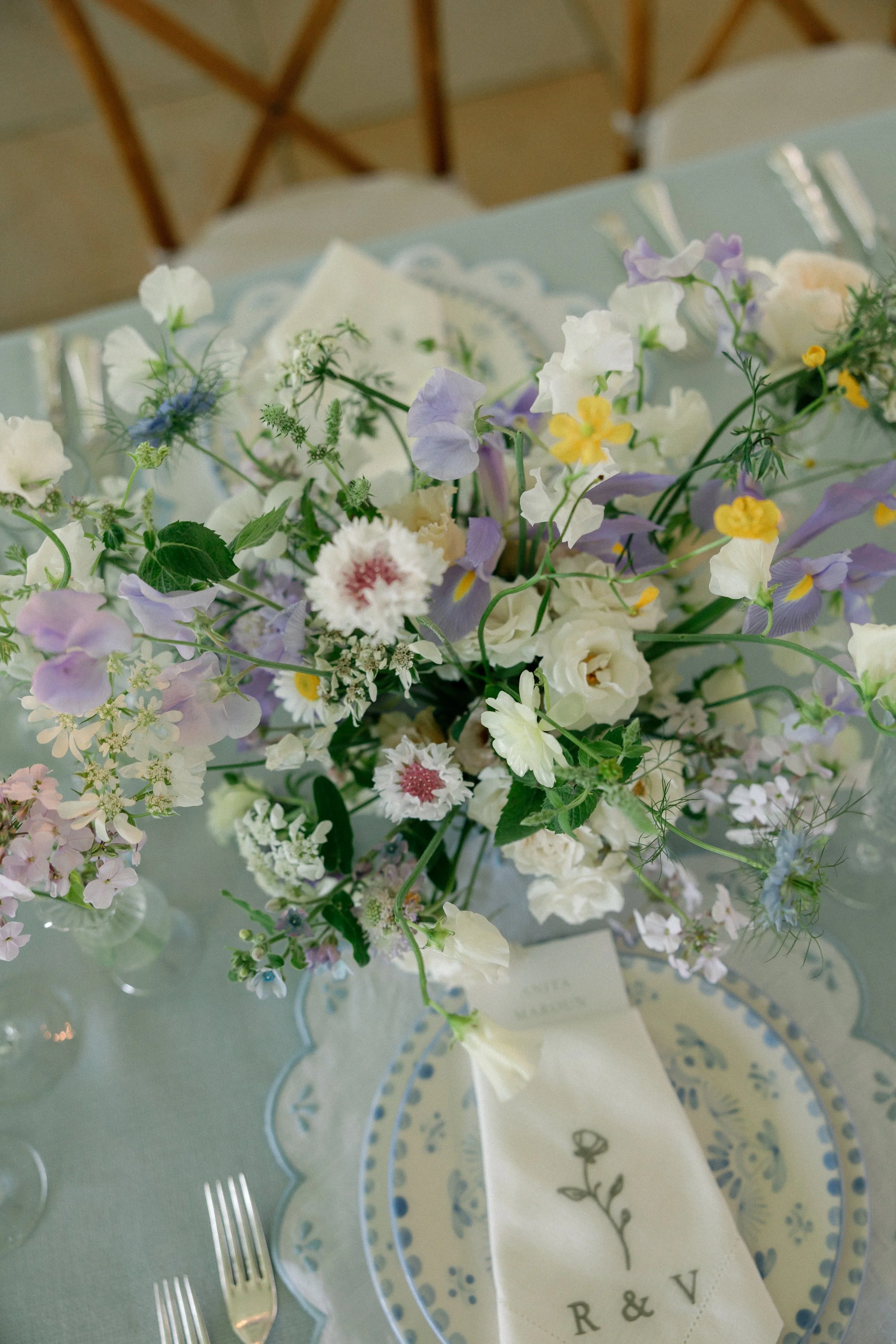 A floral centerpiece with white, purple, and yellow flowers on a table set for a special occasion or event.