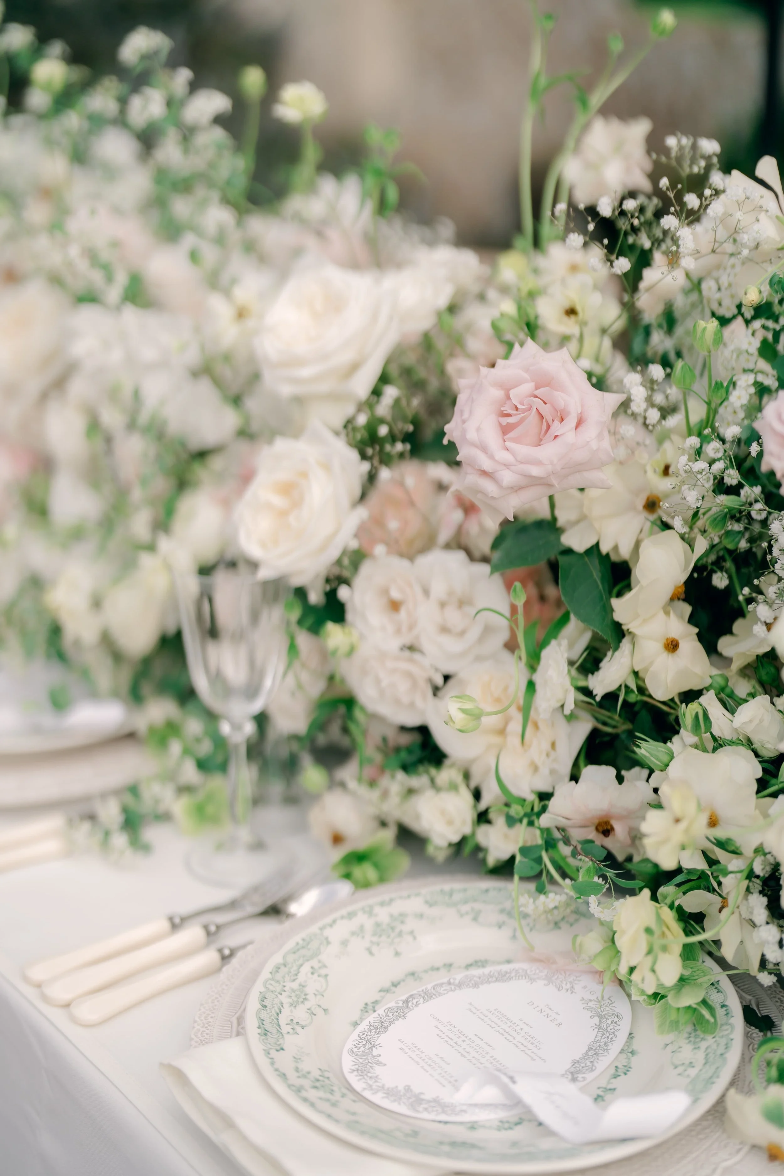 Elegant table setting with white and blush pink roses, greenery, a floral centerpiece, and ornate green and white patterned plates at Sudeley Castle in the Cotswolds