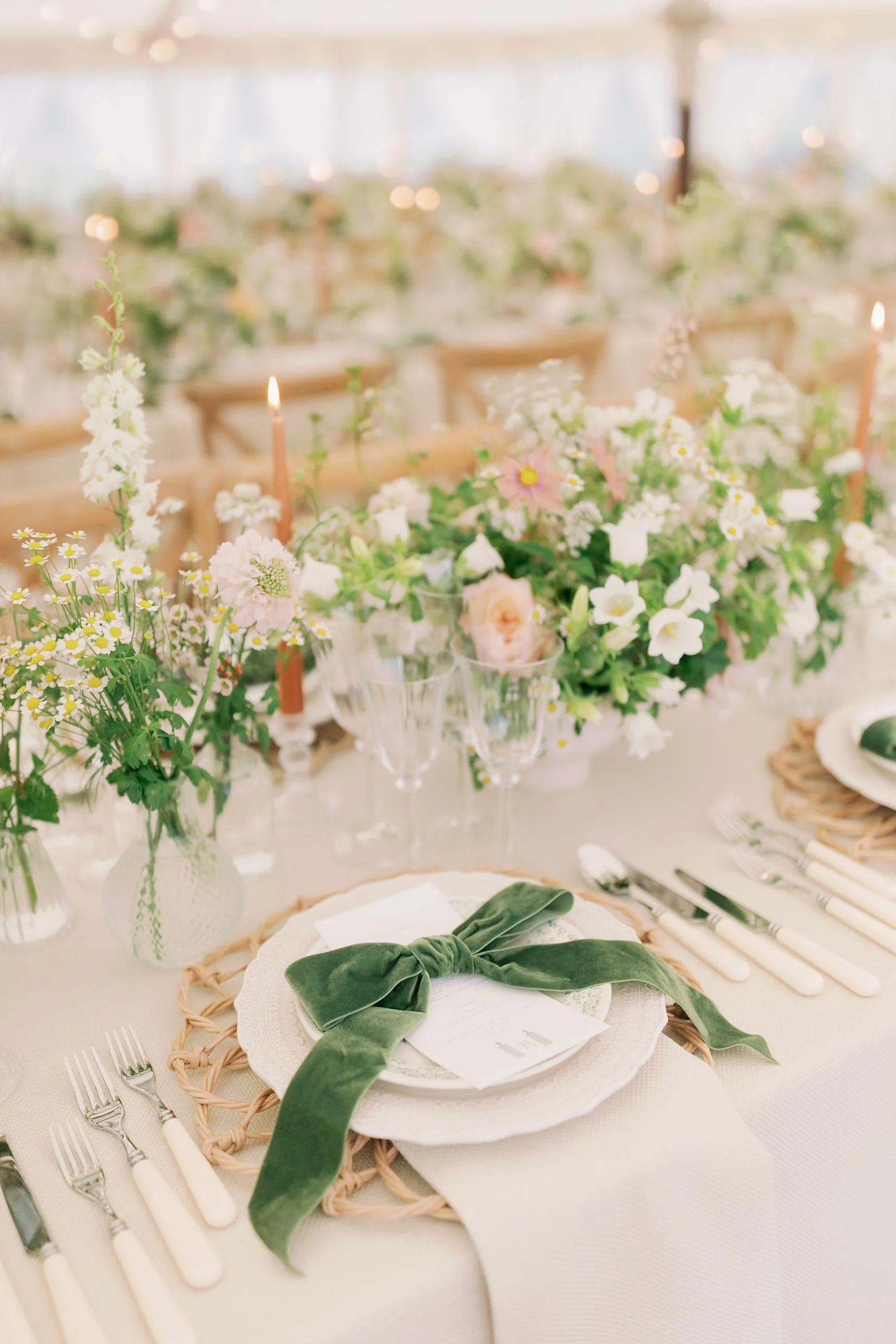 Elegant banquet table setup with floral centerpiece, white plates, green velvet ribbon, and multiple sets of cutlery.