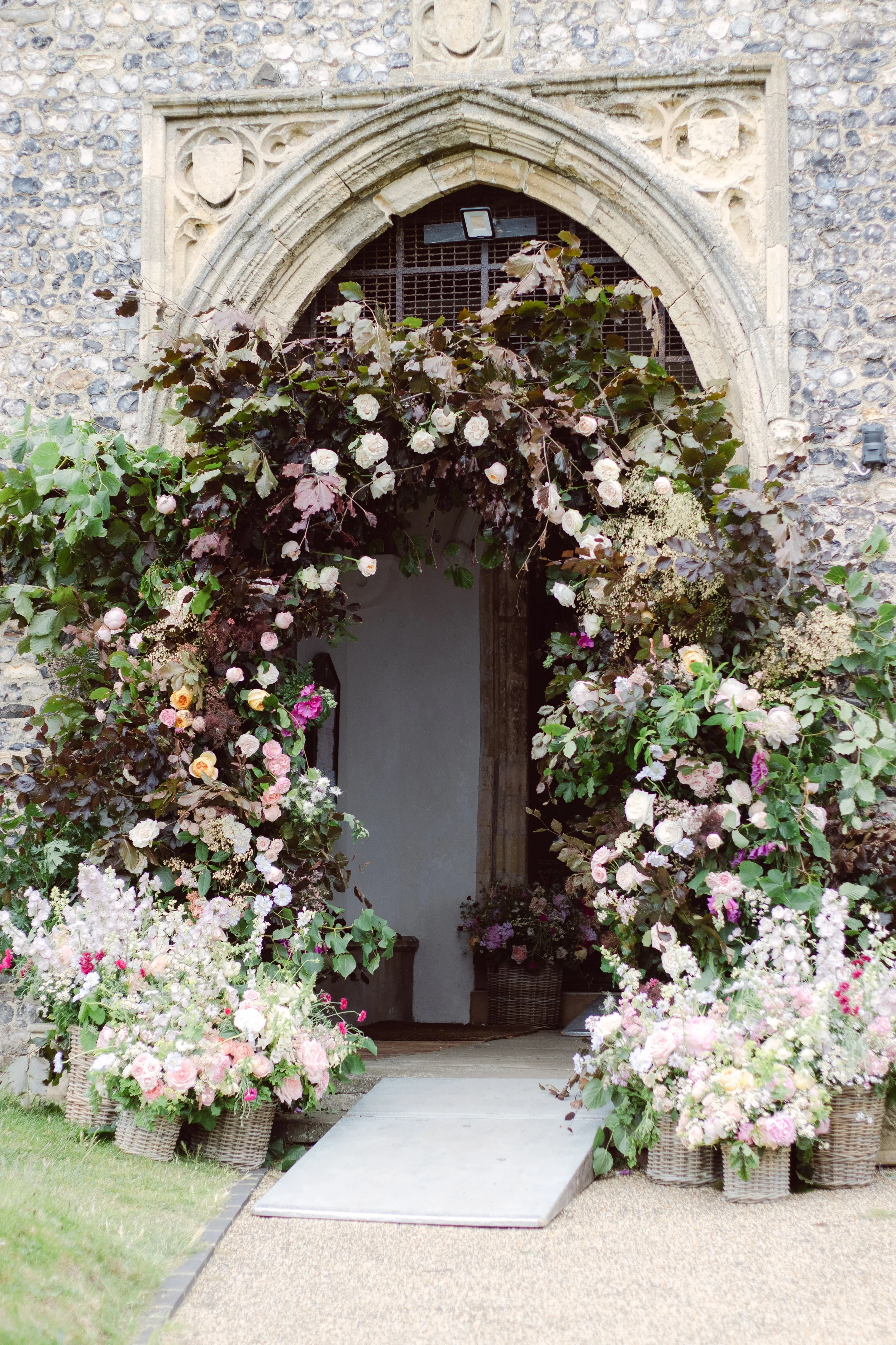 Church entrance decorated with an arch of pink and white flowers and potted flower arrangements on either side.