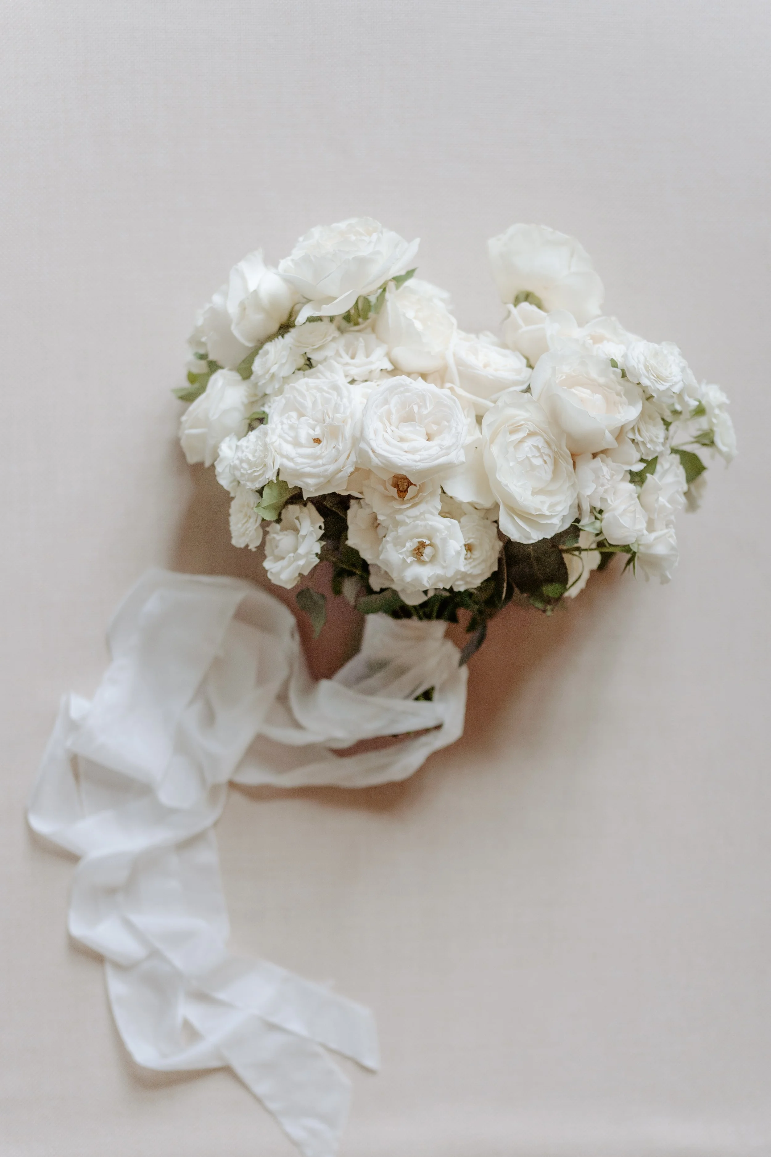 A bouquet of white roses and other white flowers tied with a white ribbon.
