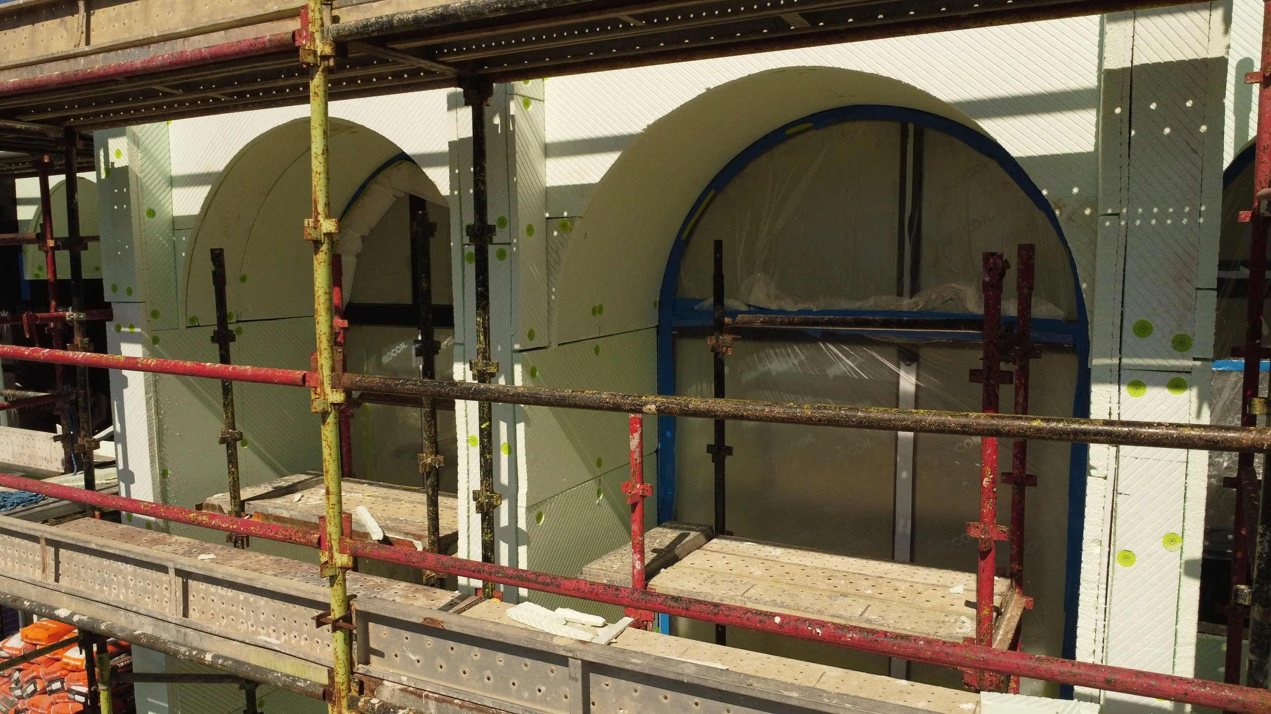 Scaffolded façade under construction showing arched openings and external wall installation