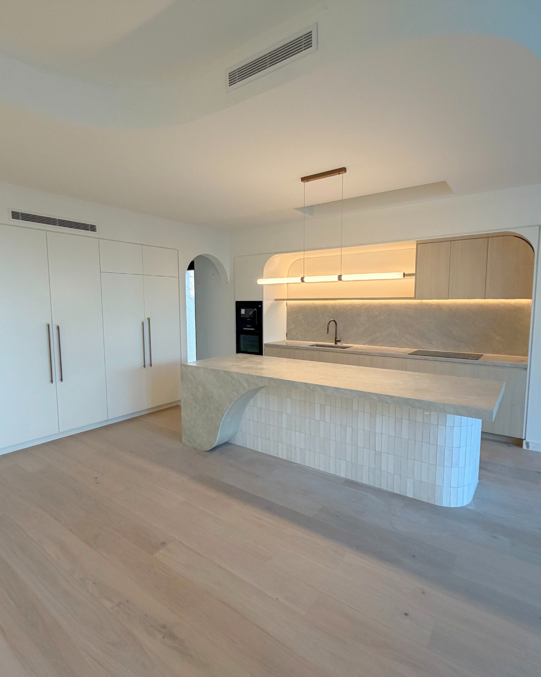 Modern kitchen in a Haymet Street duplex with curved stone island, integrated joinery, and warm lighting nearing completion