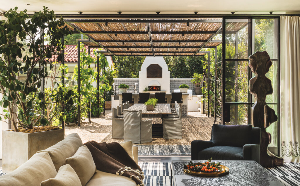  Custom luxury estate general contracting company Spanish Colonial California residence in the Beverly Hills neighborhood of Los Angeles featuring Bohemian eclectic outdoor living room with straw roof and lush landscaping.  