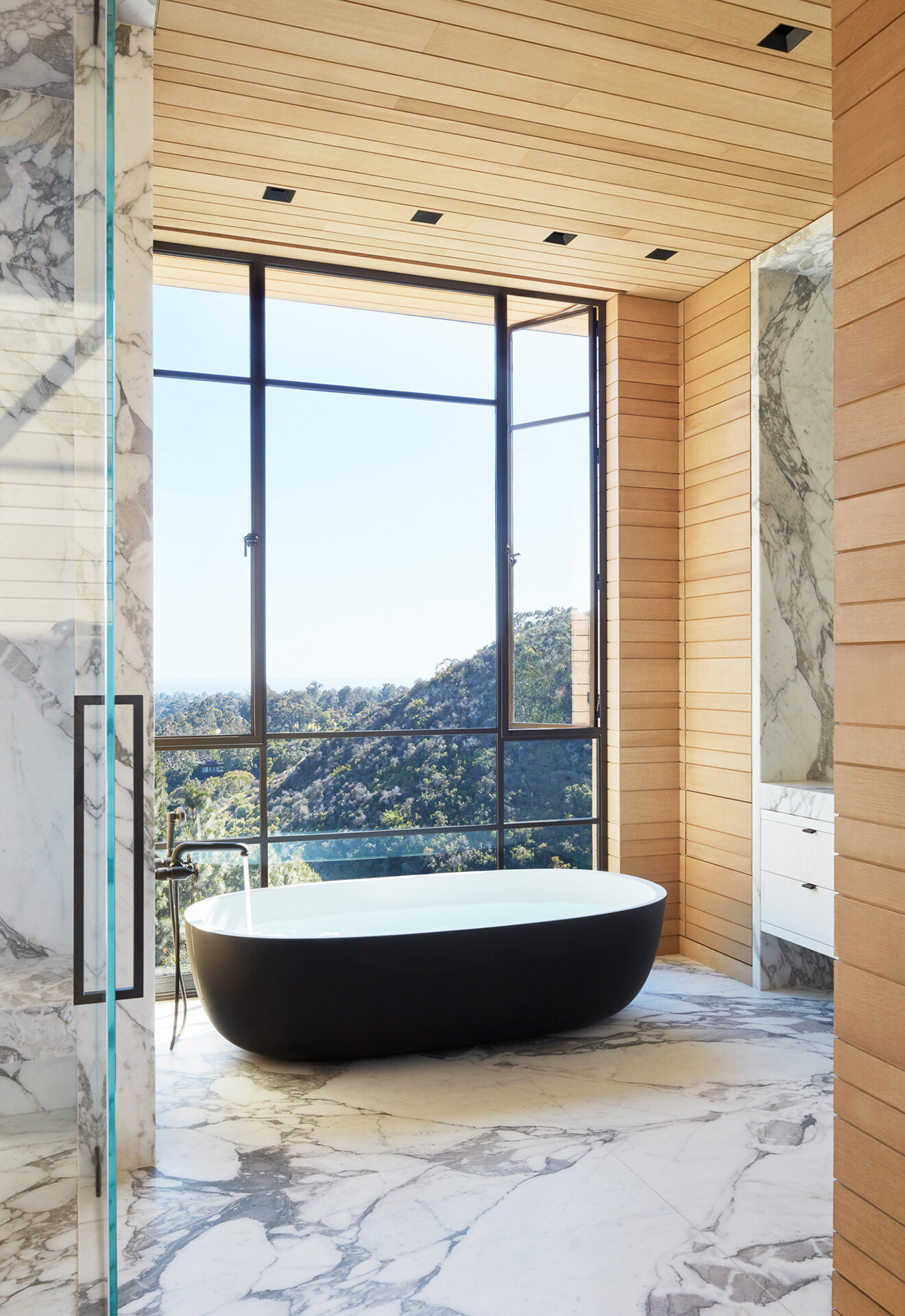  Custom luxury home general contractor built modern private residence in the Pacific Palisades neighborhood of Los Angeles featuring glamorous master suite bathroom with freestanding matte black bathtub and bold marble walls.  