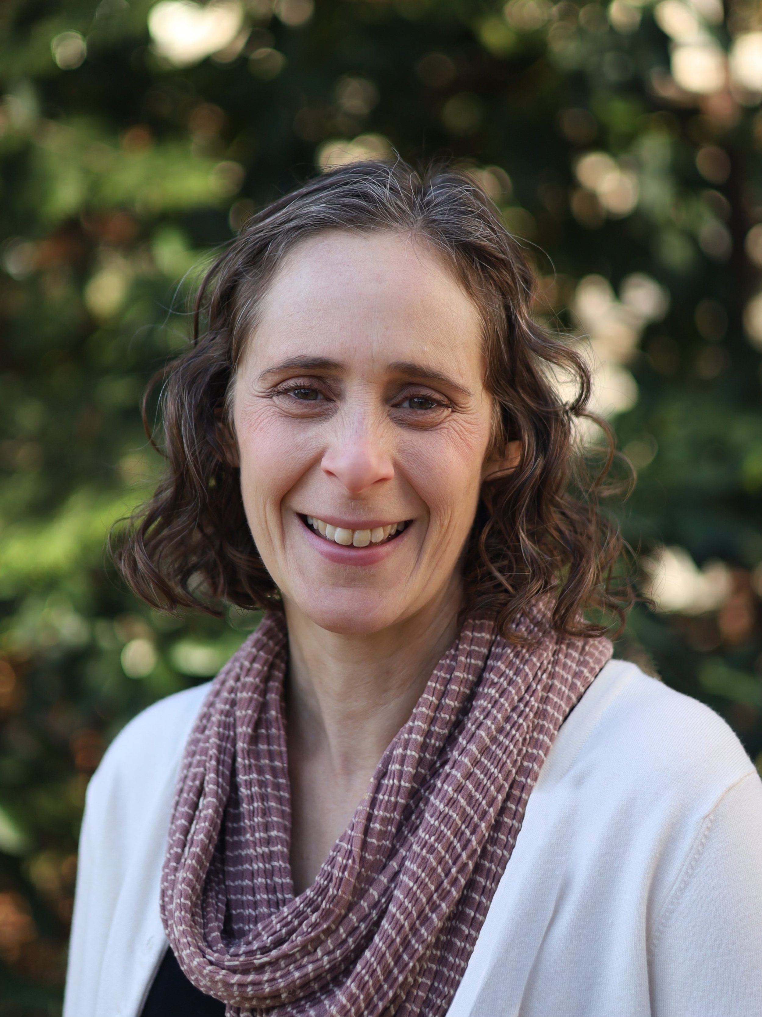 Melissa Baird, trauma therapist at All of You Therapy in Philadelphia, white woman with wavy brown hair wearing a scarf and smiling at the camera