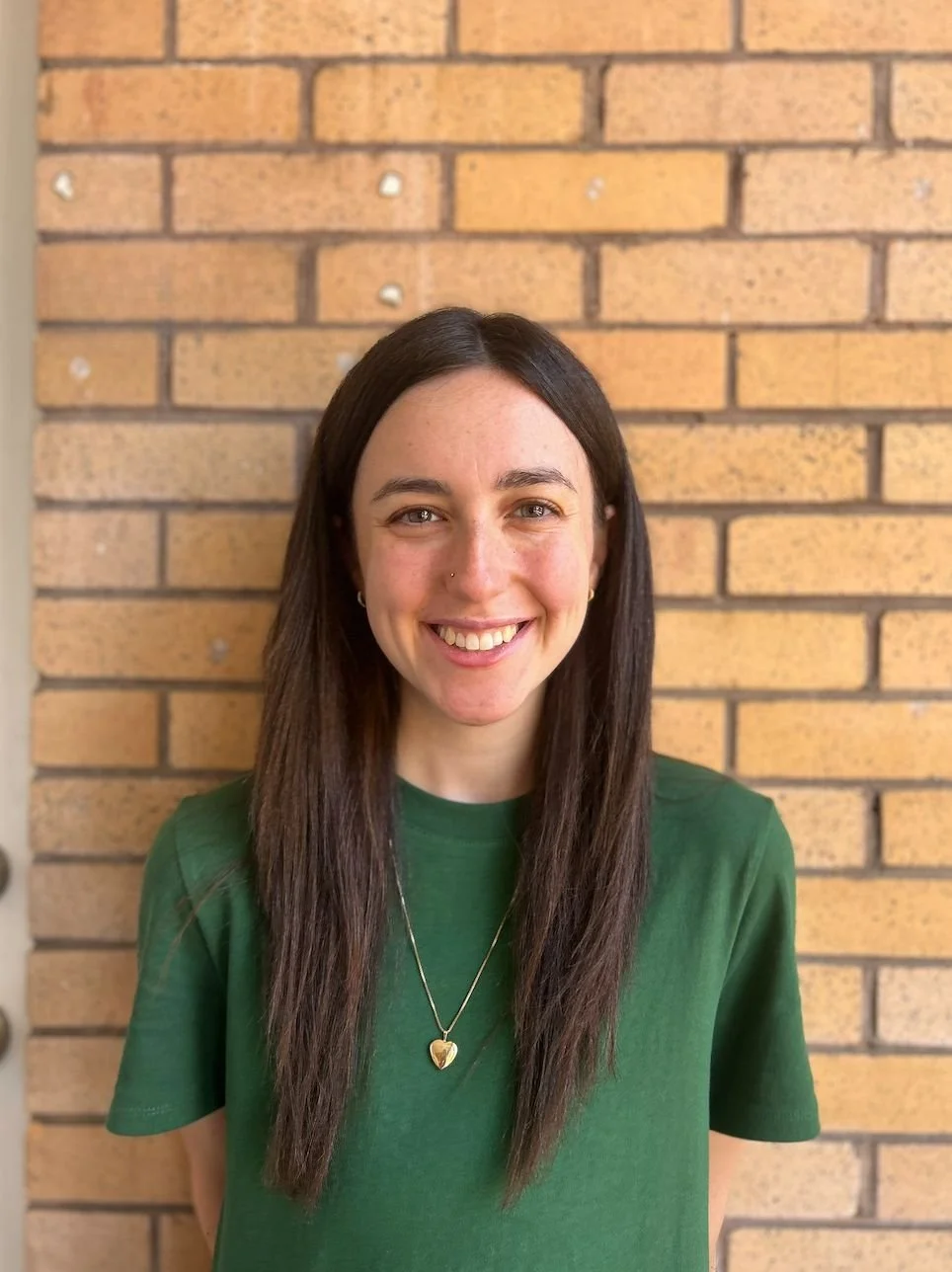 Leah Welde, therapist at All of You Therapy, standing in front of a brick wall, wearing a green long sleeve shirt, smiling at the camera