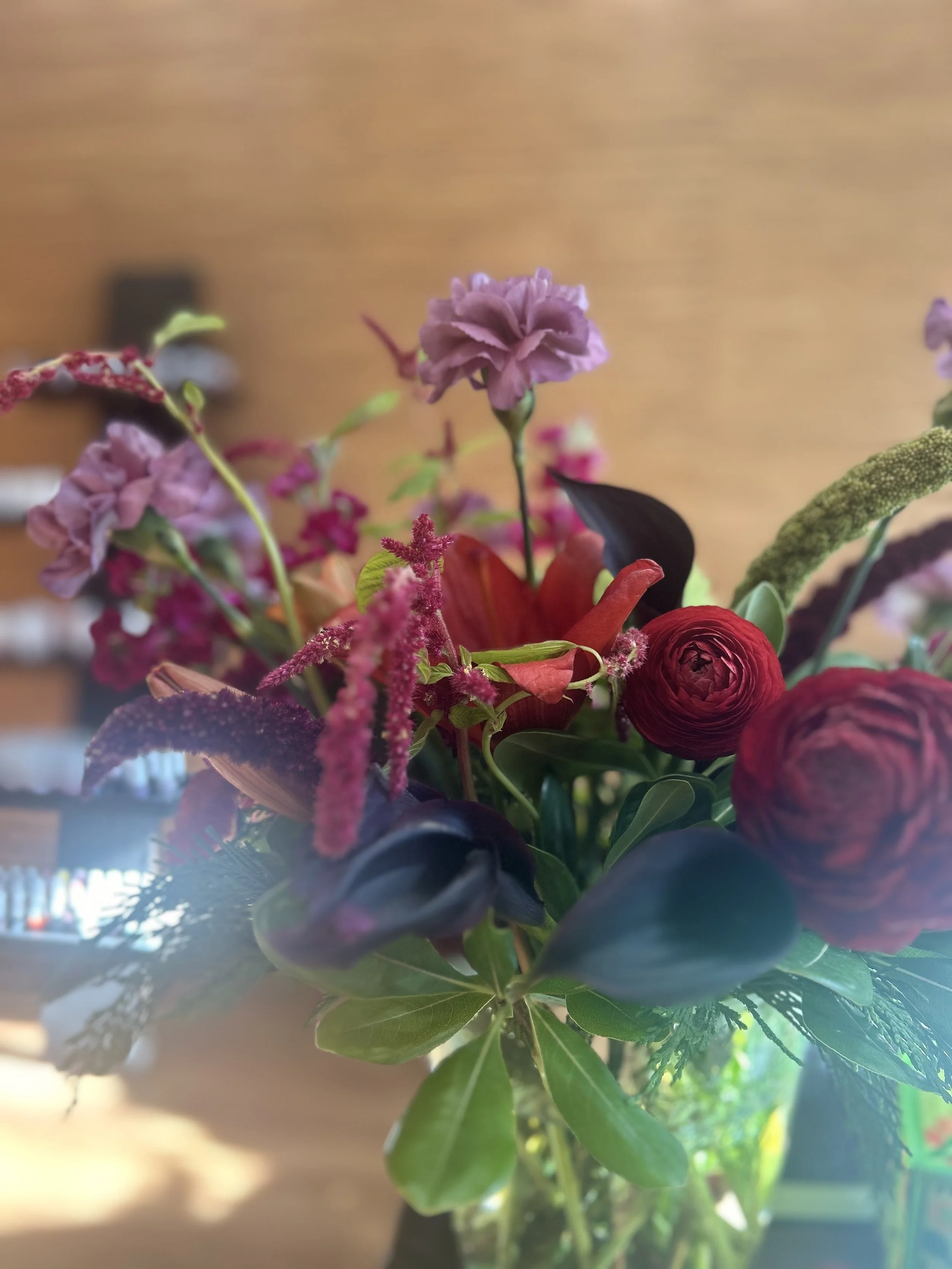 A close-up of a colorful flower arrangement with purple and red blooms, green leaves, and a blurred background.