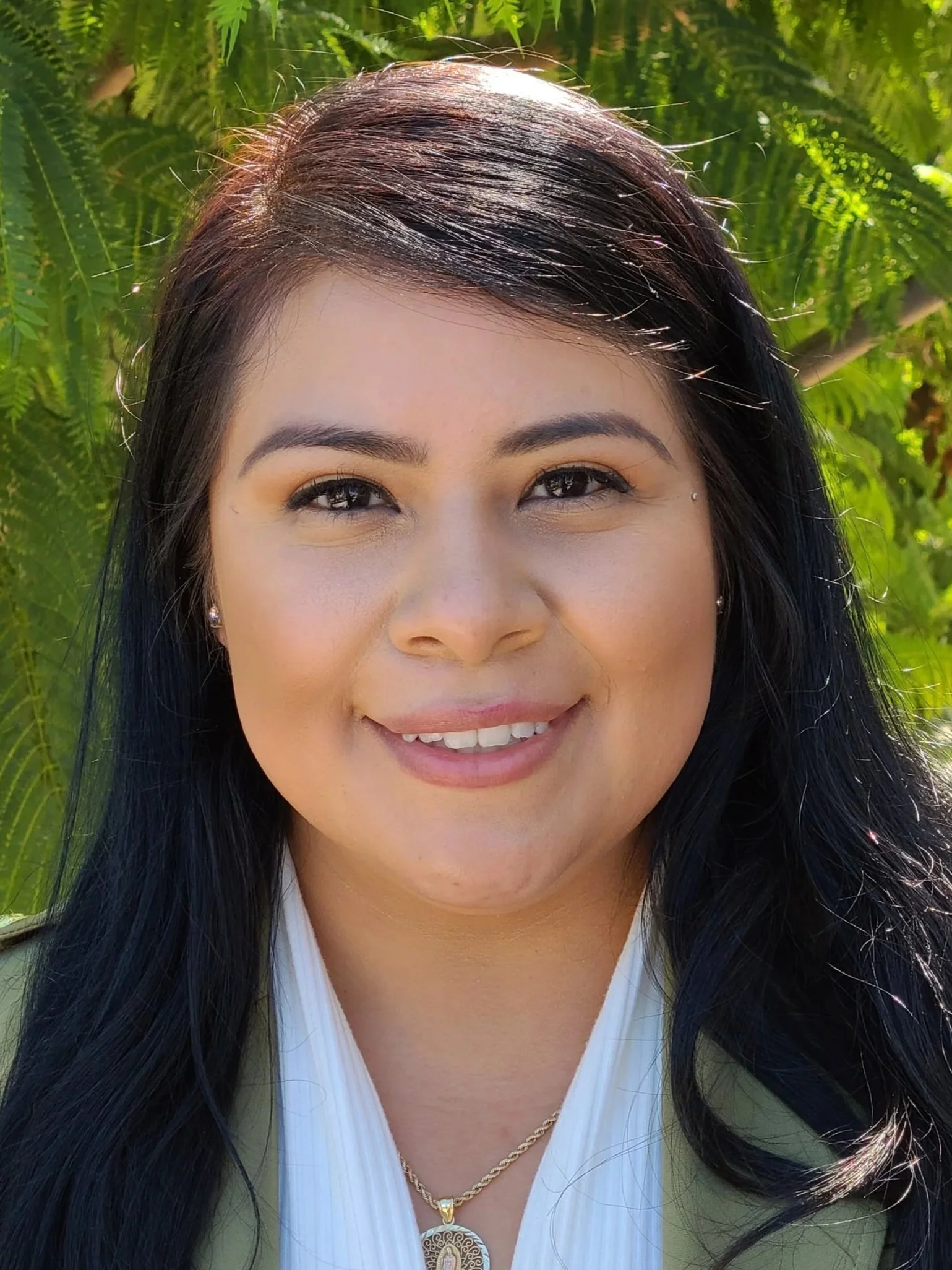 A woman wearing a green coat and white shirt standing in front of a tree