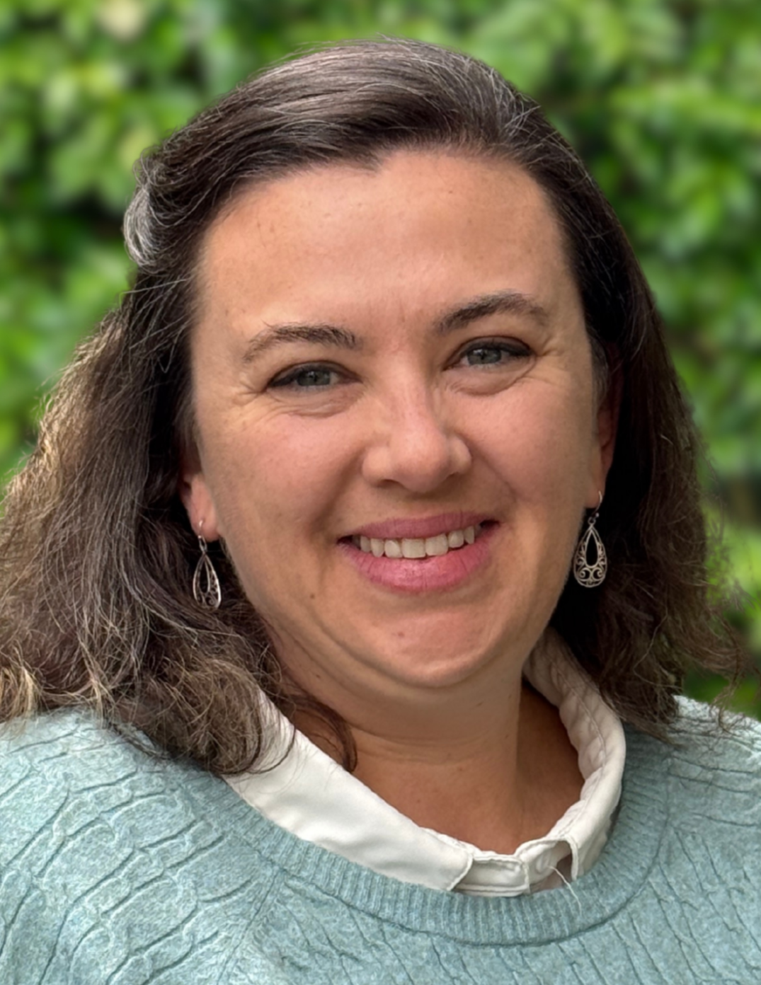 A smiling woman wearing a green sweater posing for a photo in front of green shrubbery
