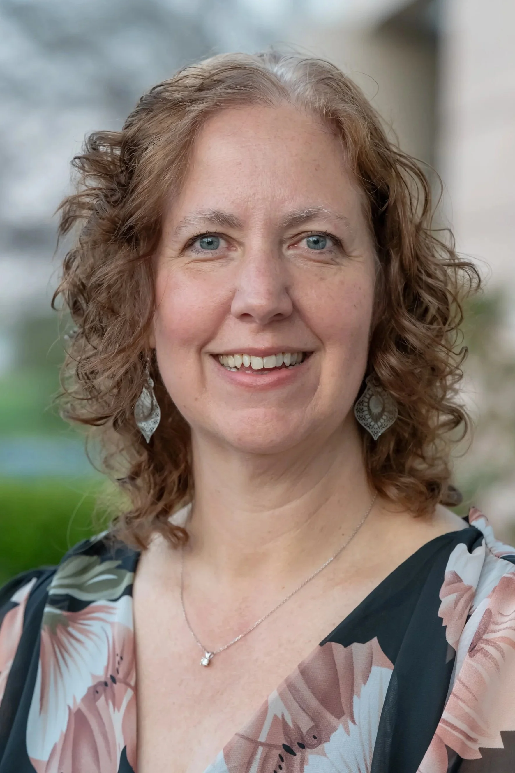 A smiling woman wearing a floral outfit posing for a photo while standing outside
