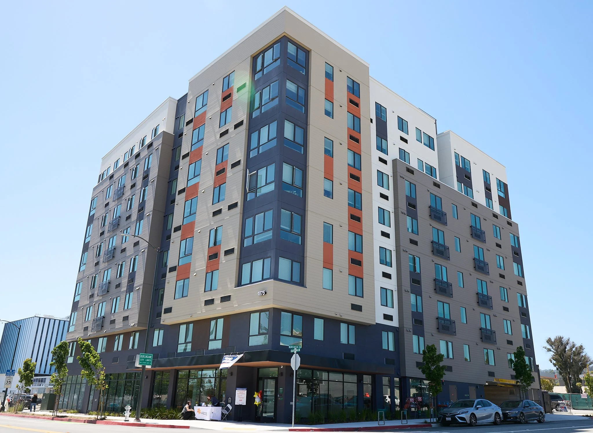 An exterior photo shows an 8-story affordable housing complex standing in the city of Burlingame, with two cars parked on the street next to the building