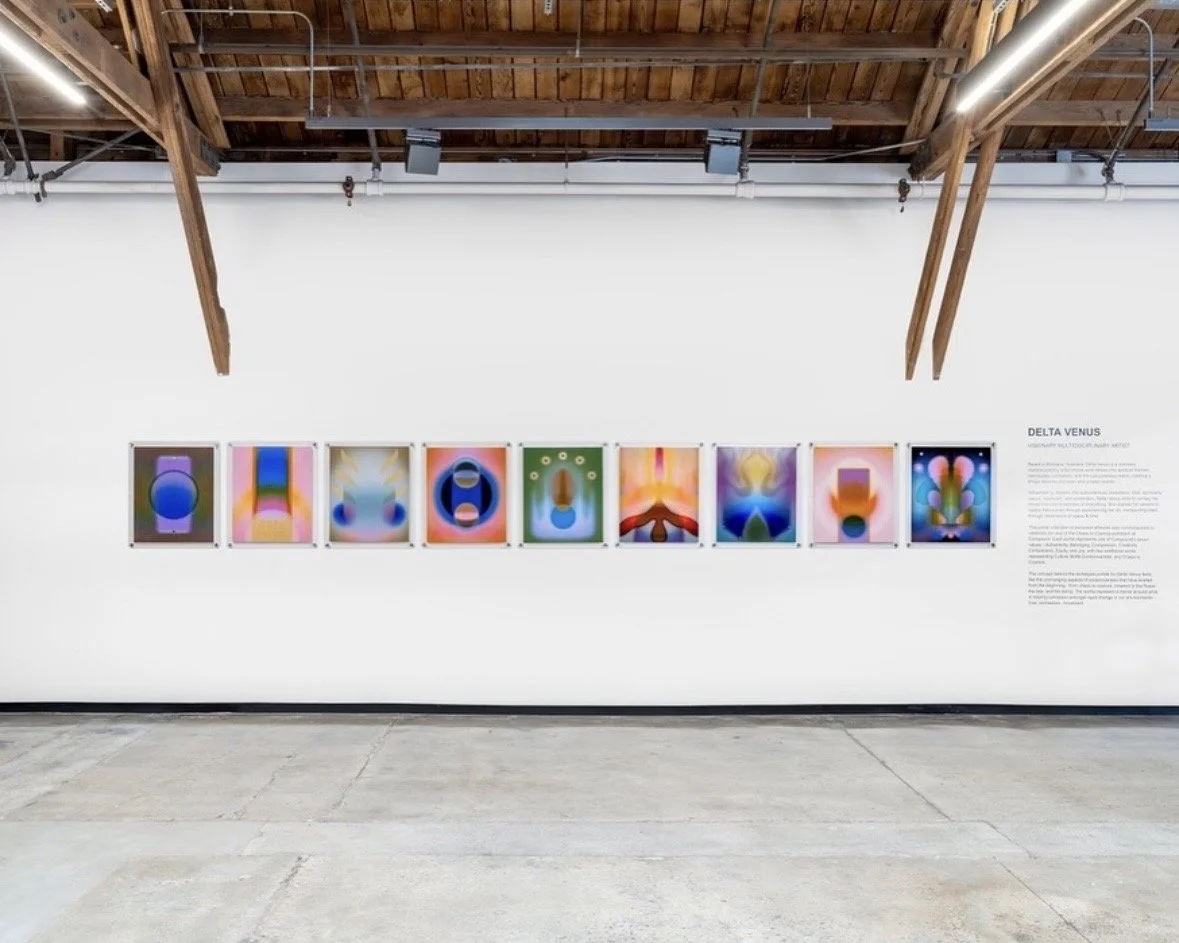 Nine colorful art prints mounted to a white wall with wall text in a warehouse setting